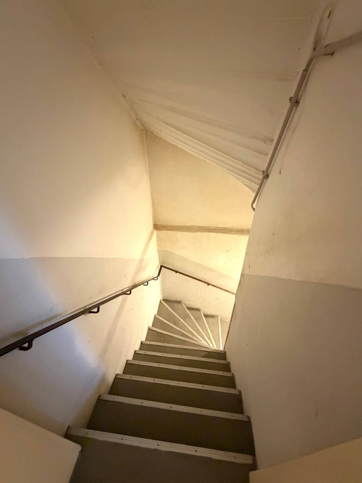 Enges Treppenhaus mit Teppichstufen und Handlauf, führt in die obere Etage.