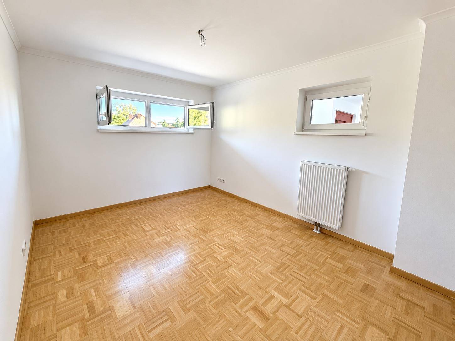 Helles Schlafzimmer mit Parkettboden und zwei Fenstern, bereit zur individuellen Gestaltung.