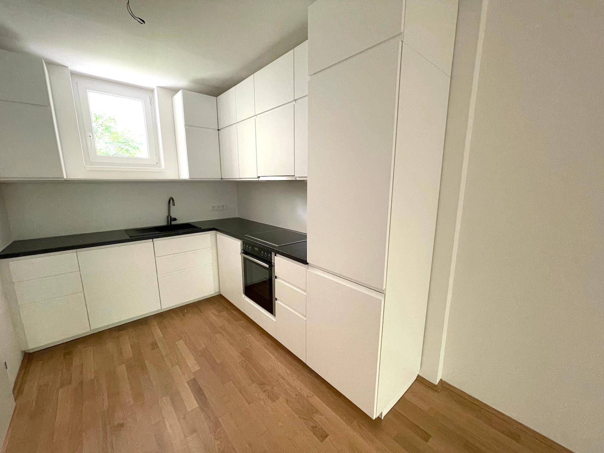 Moderne, unmöblierte Küche mit weißen Schränken, dunkler Arbeitsplatte und integriertem Backofen.