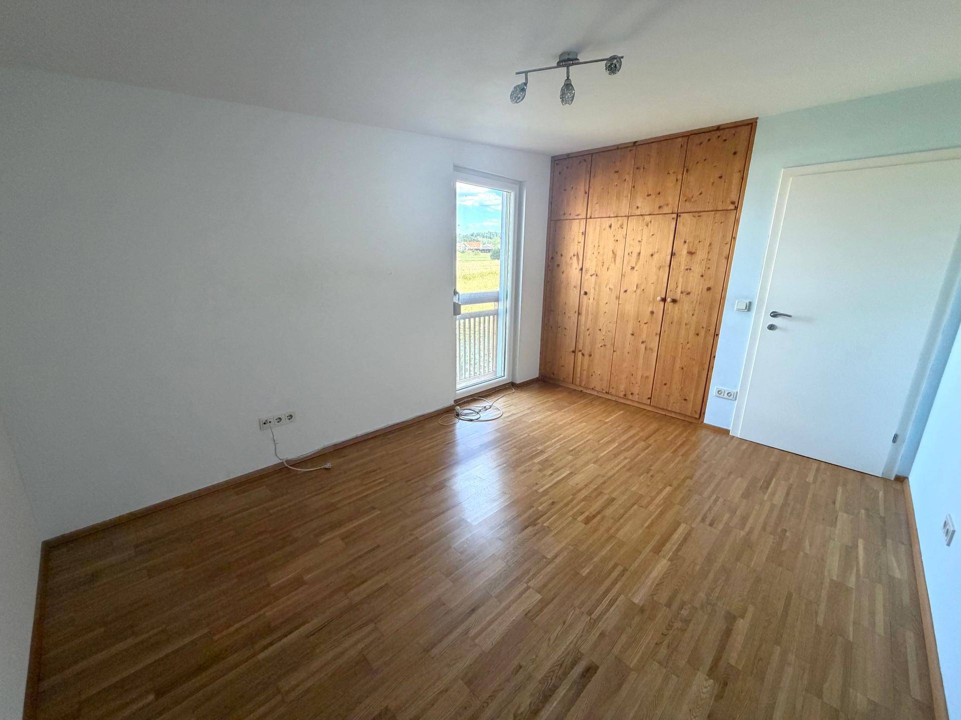 Schlafzimmer mit Holzboden, Einbauschrank und Zugang zu einem französischen Balkon.