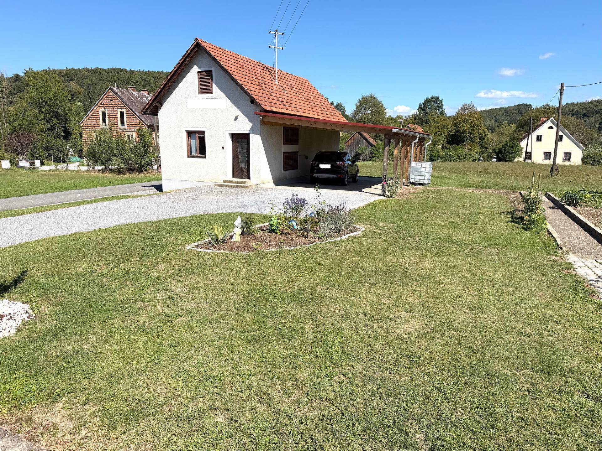 Kleines Einfamilienhaus mit Carport, Kiesauffahrt und gepflegtem Garten in ländlicher Umgebung.