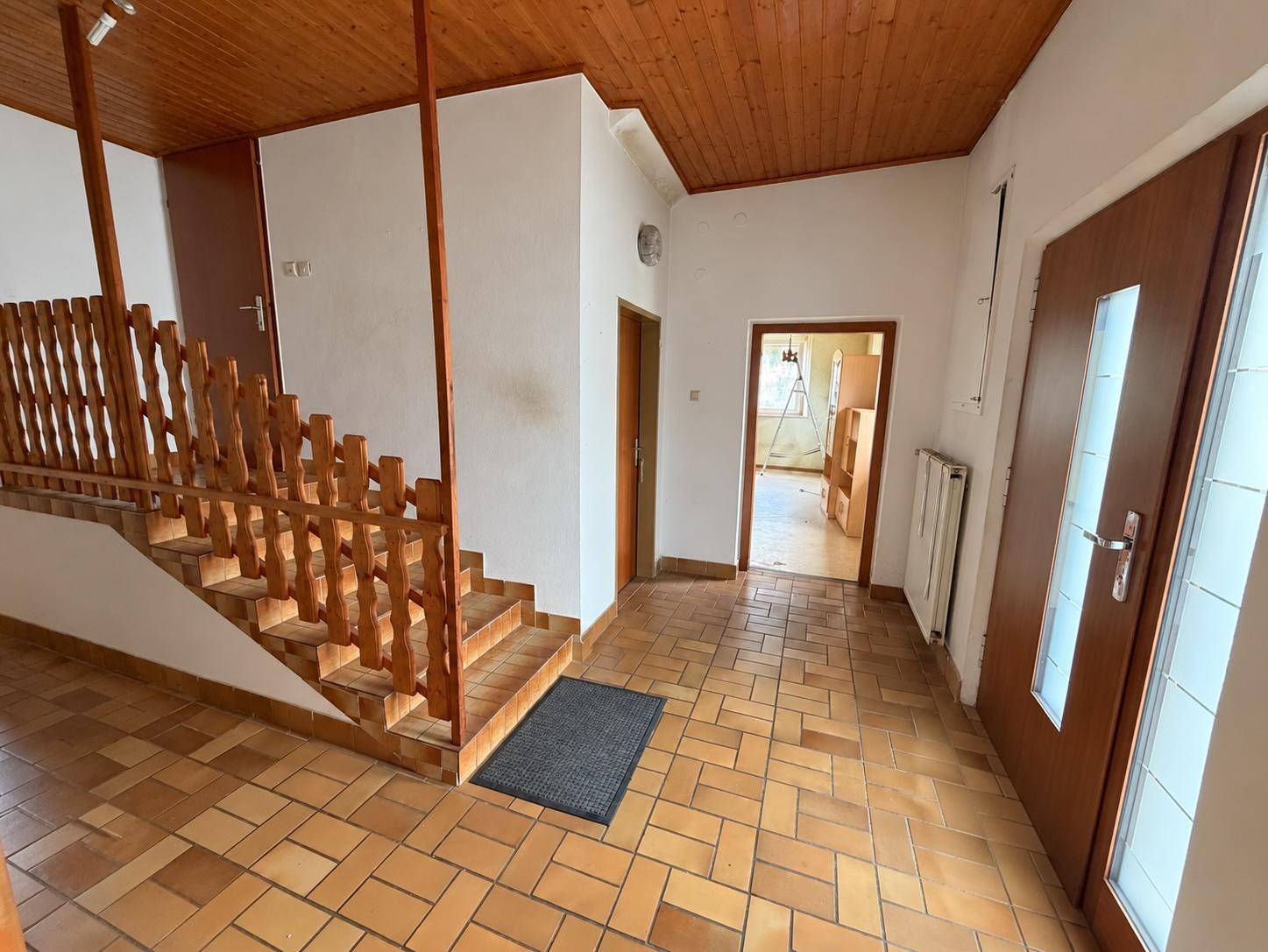Eingangsbereich mit Holztreppe, Terrakottafliesen und Holzbalkendecke.
