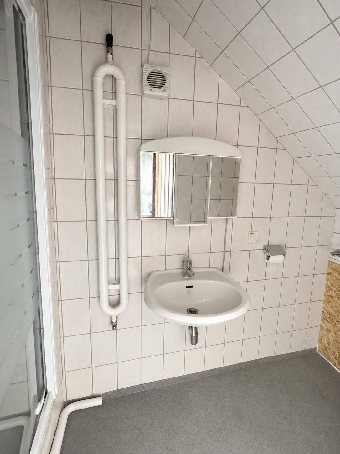 Helles Badezimmer im Dachgeschoss mit Waschbecken, Spiegel und Duschkabine.