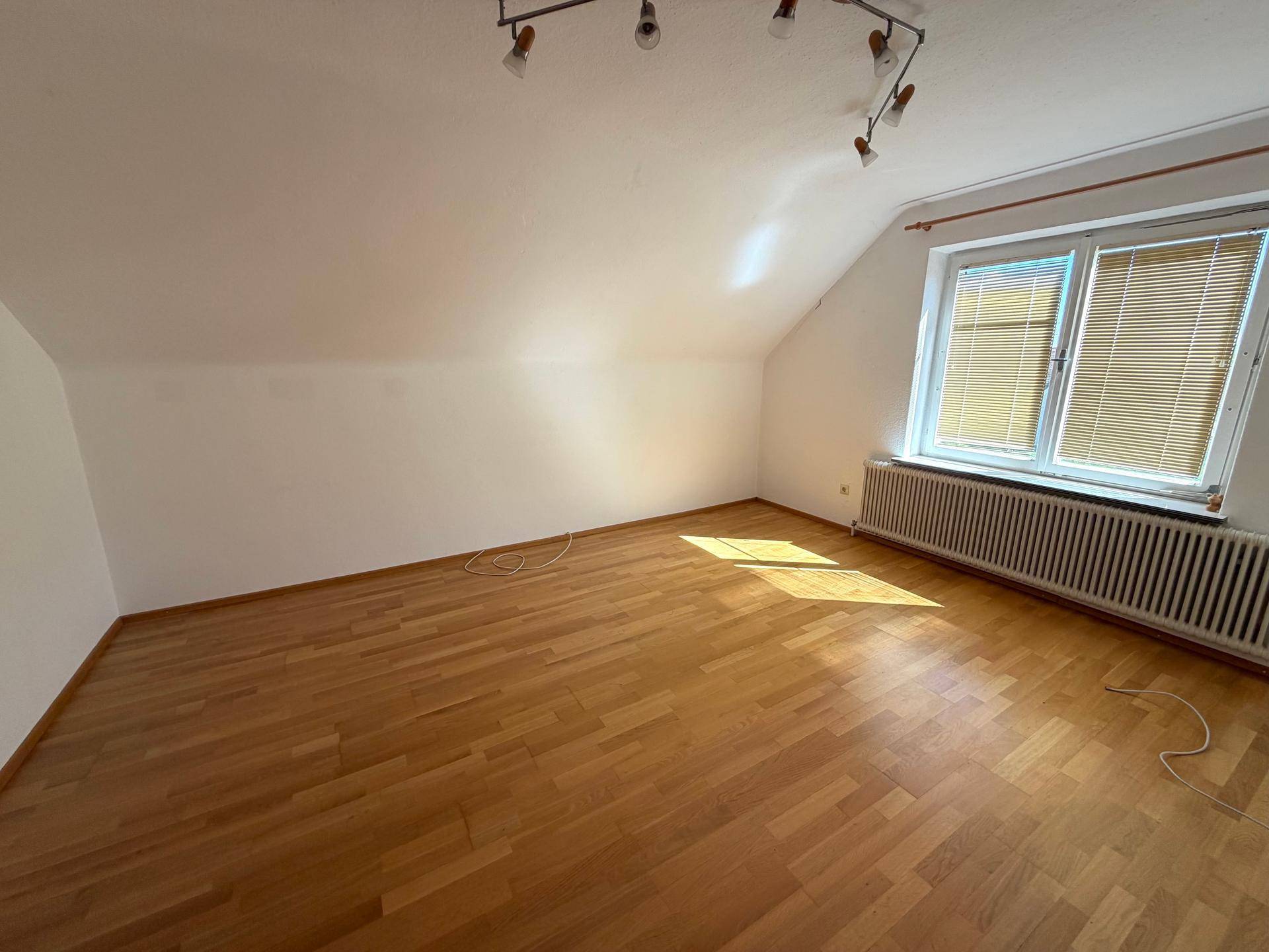 Geräumiges Schlafzimmer im Dachgeschoss mit Holzboden, Fenster und Heizkörper.