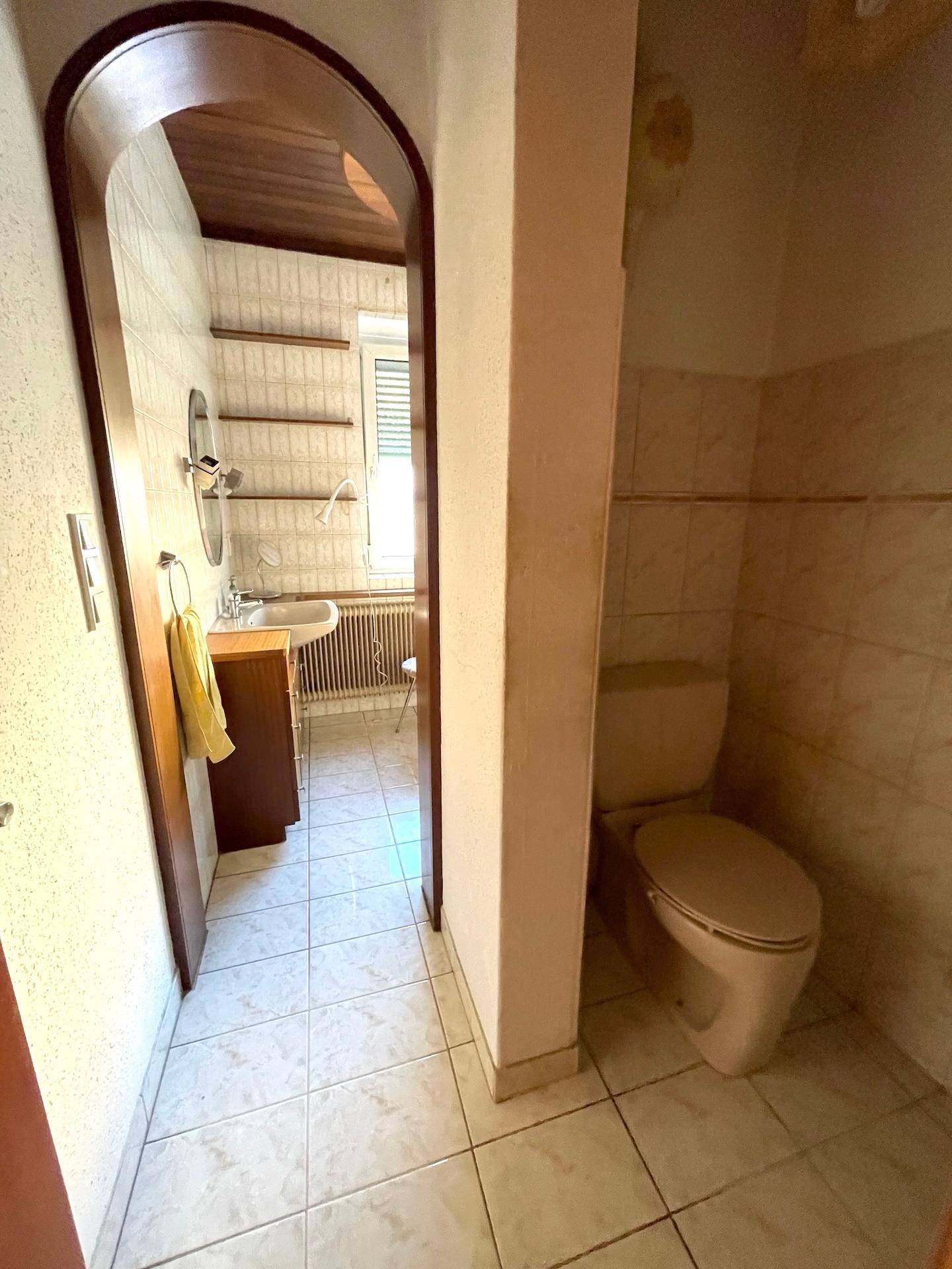Badezimmer mit Fliesenboden, Waschbecken und separatem WC-Bereich.