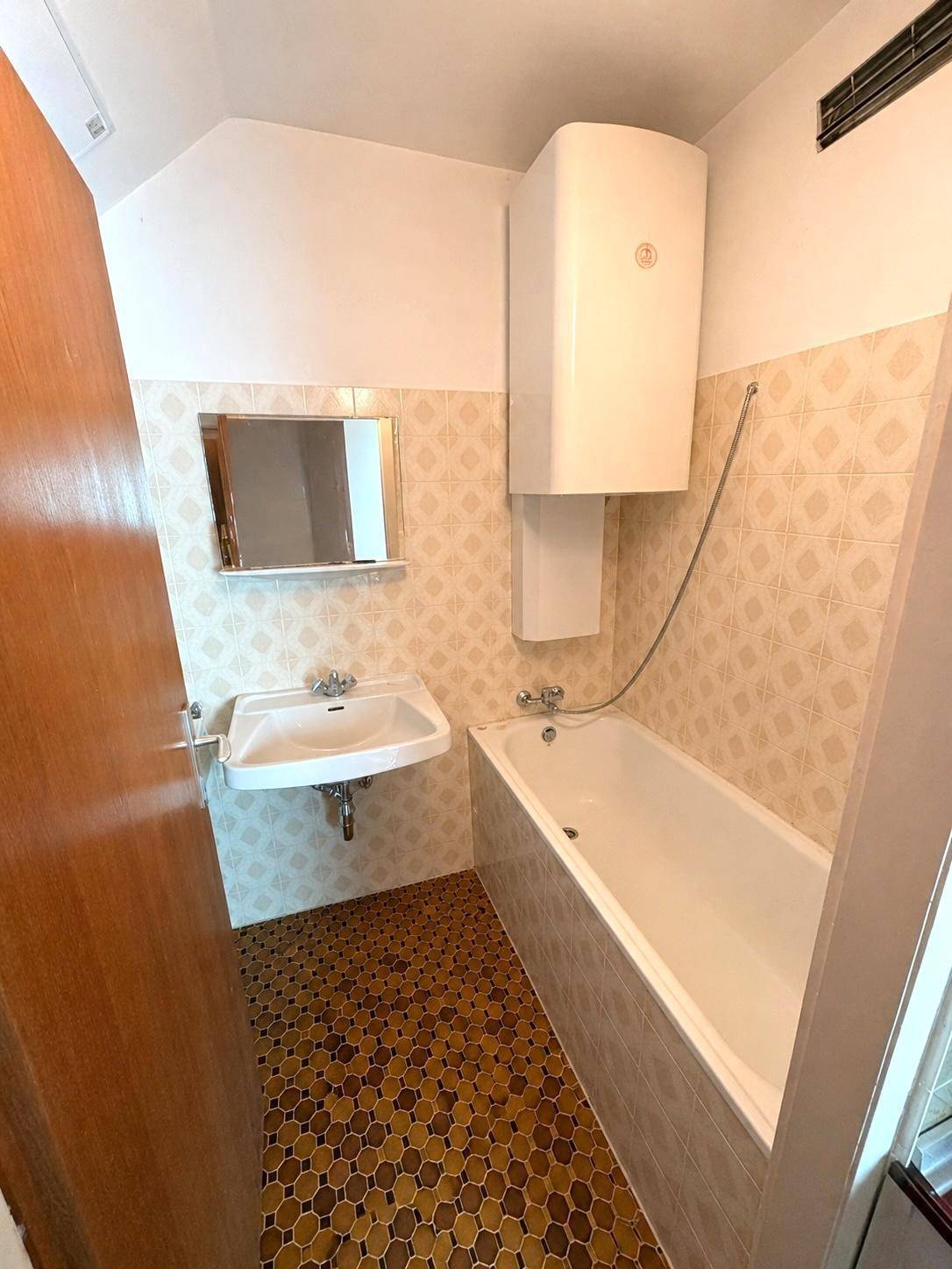 Badezimmer mit Badewanne, Waschbecken und Wandfliesen im älteren Stil.