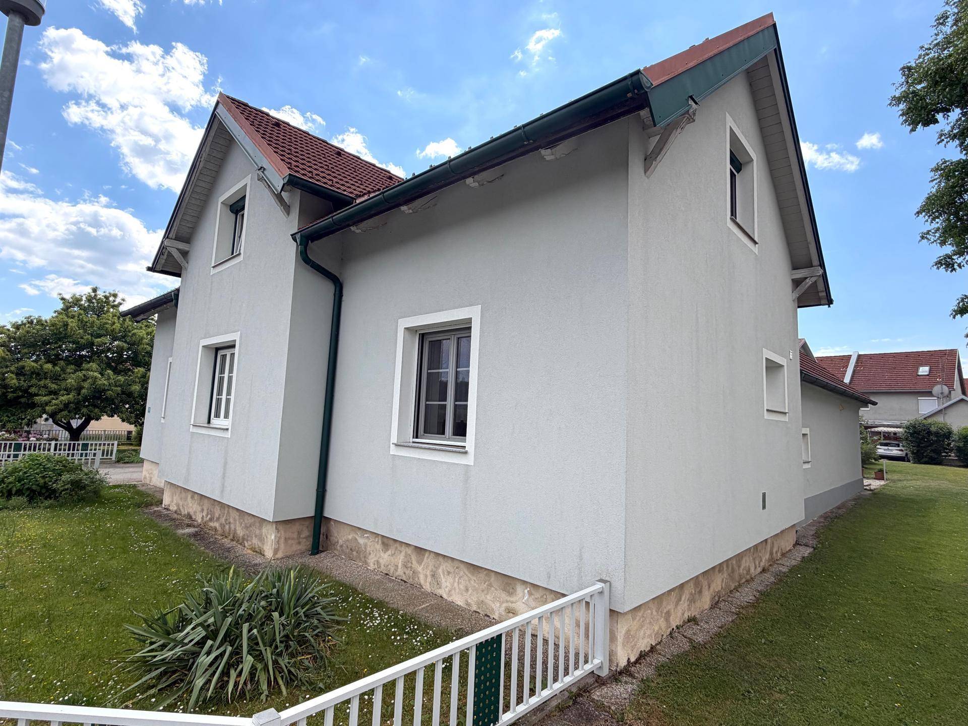 Seitenansicht des Wohnhauses mit heller Fassade, weißen Fenstern und klassischem Ziegeldach.