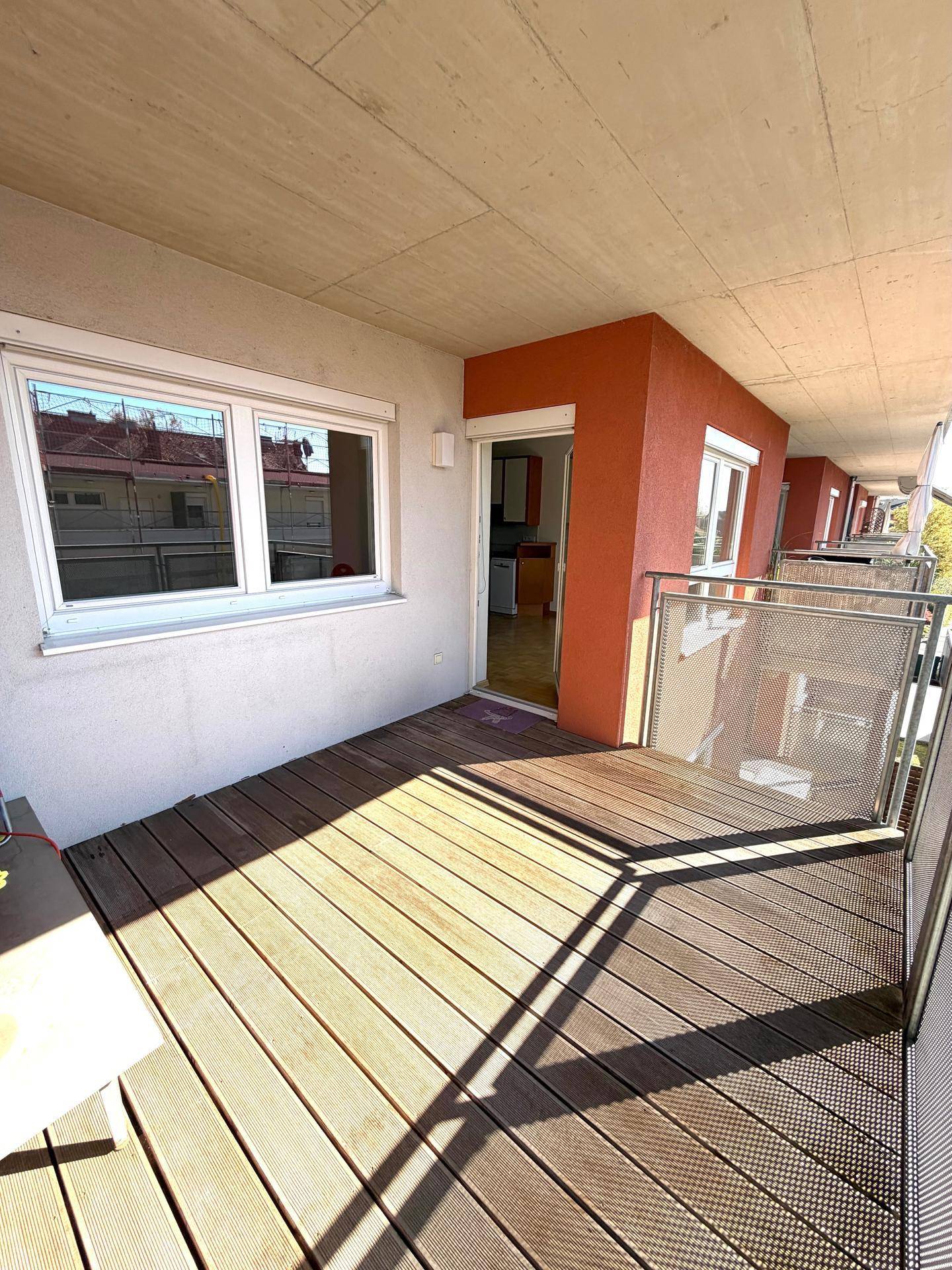 Geräumiger Balkon mit Holzdeck und direktem Zugang zum Innenbereich der Wohnung.