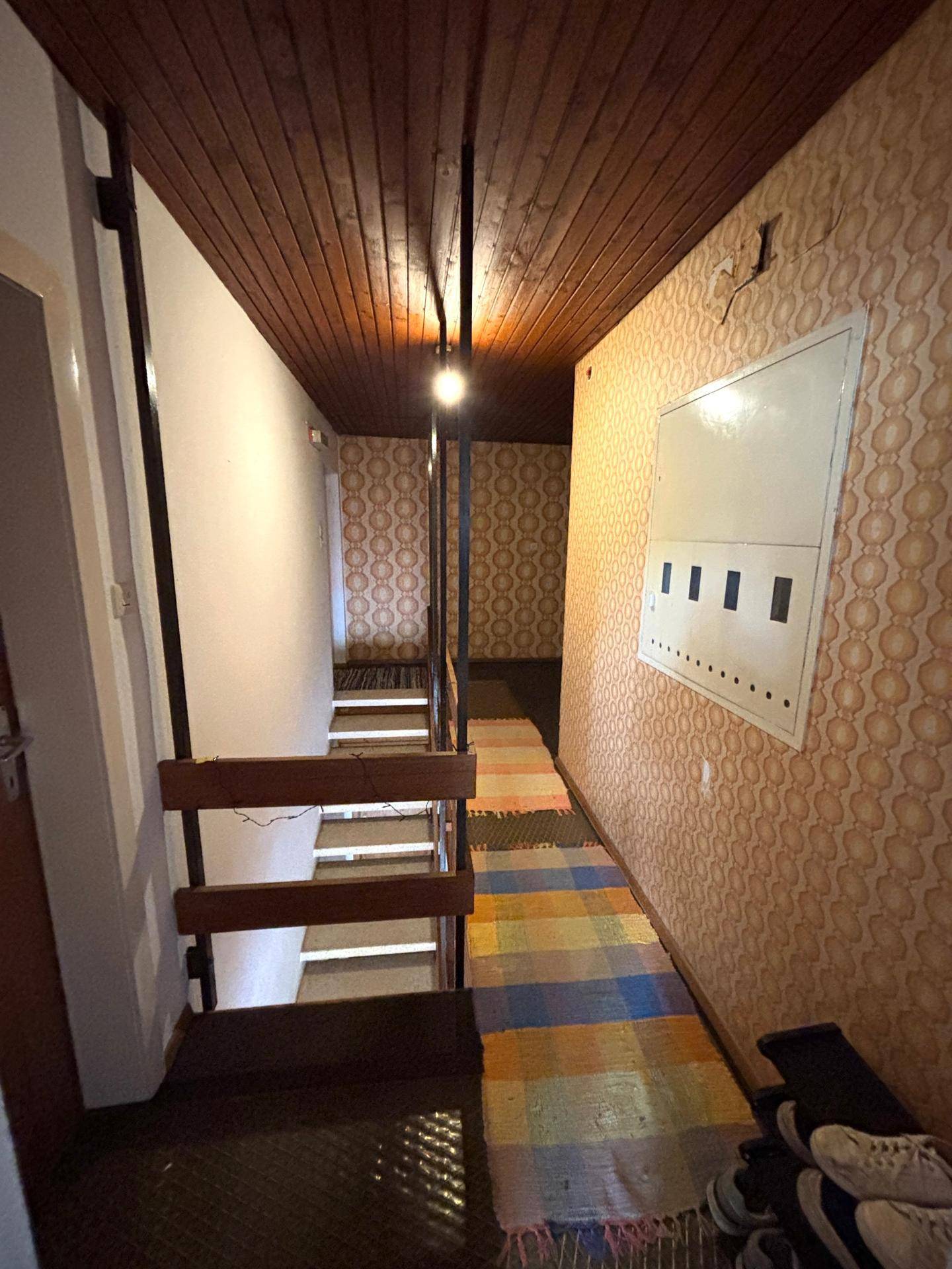 Treppenhaus mit gemusterter Tapete, Holzdecke und Teppichläufern.