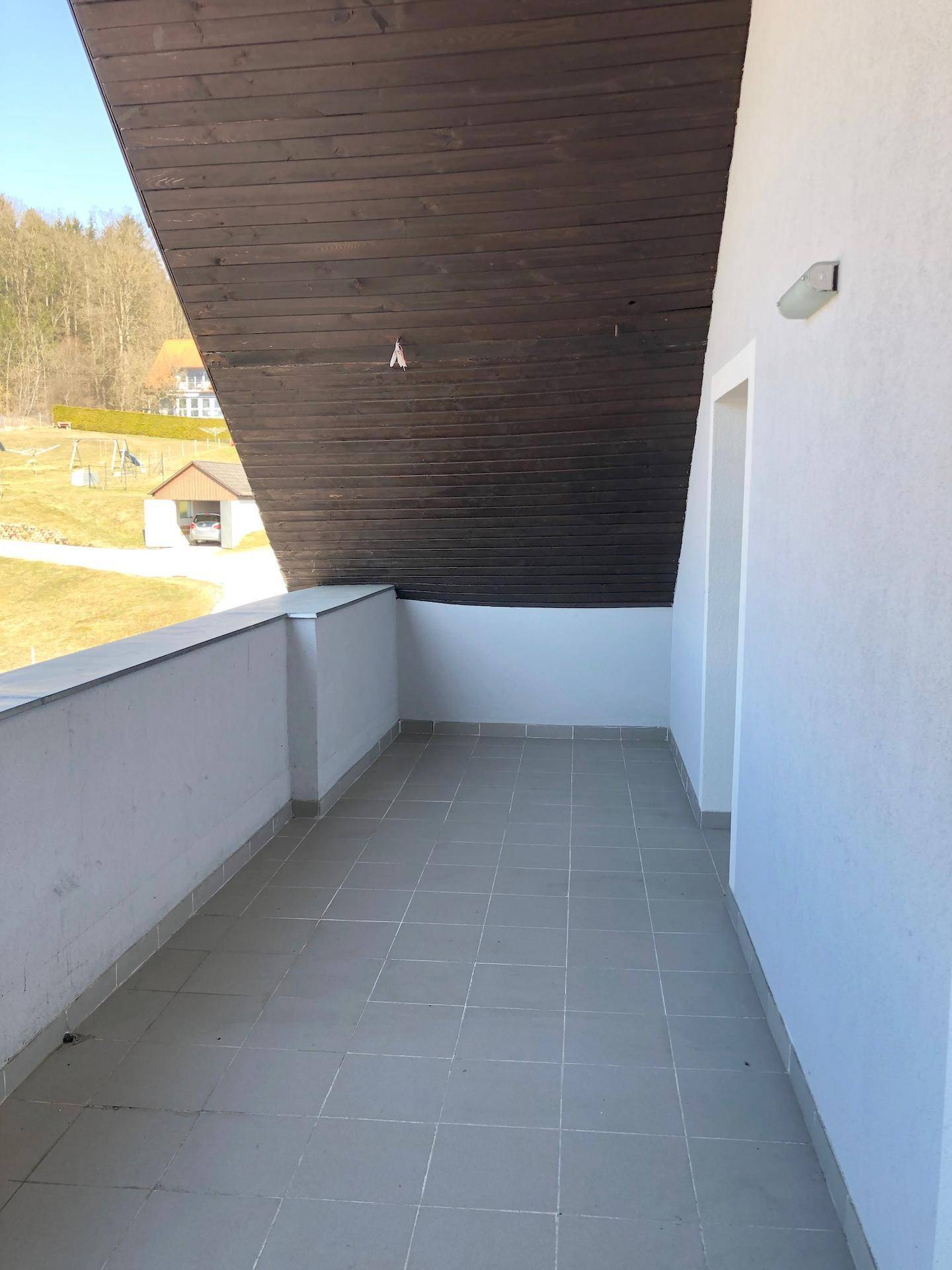 Großer Balkon mit Fliesenboden und Blick auf die grüne Umgebung.