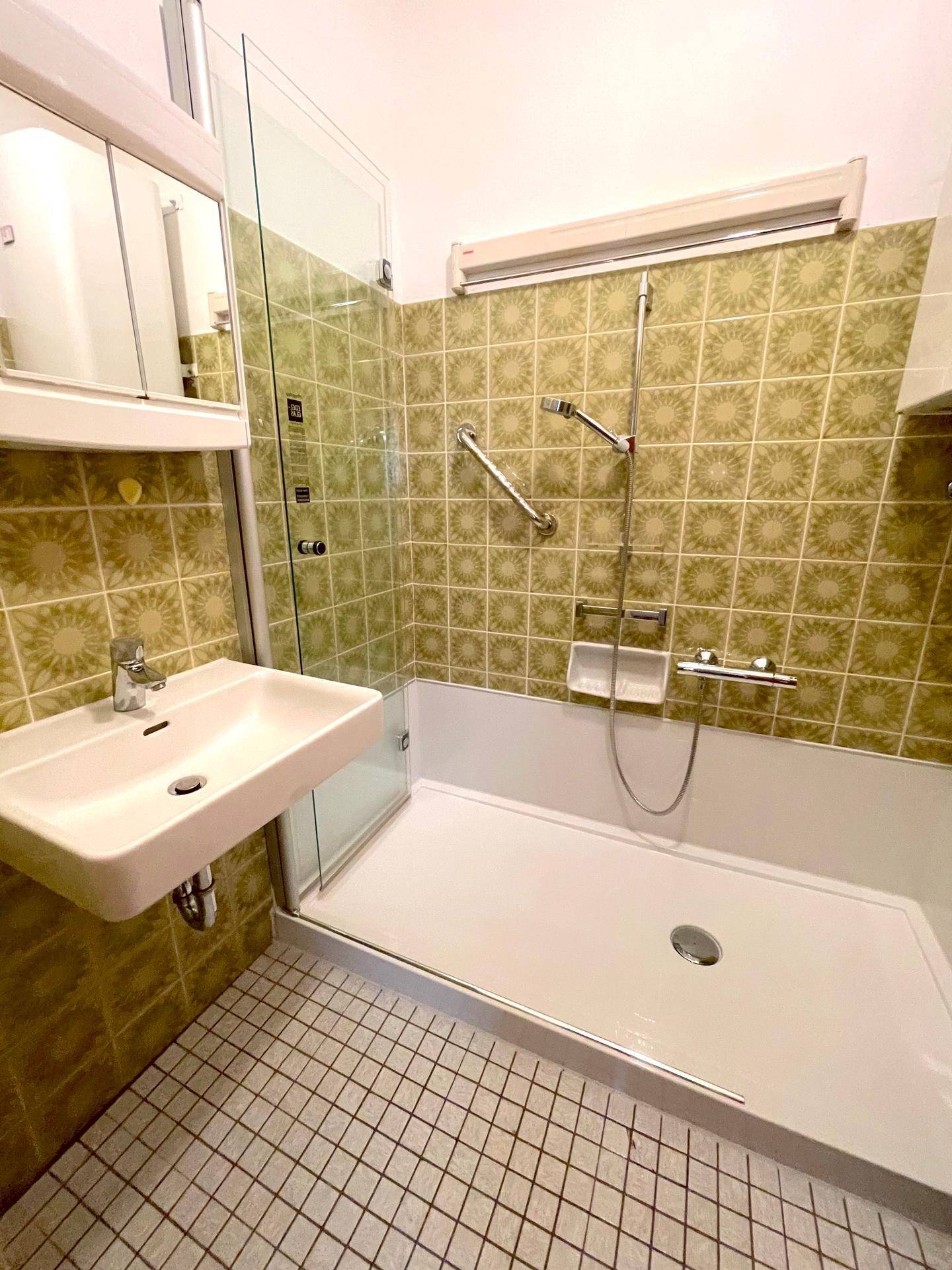 Badezimmer mit Duschwanne, Waschbecken und gemusterten Fliesen im Retro-Stil.