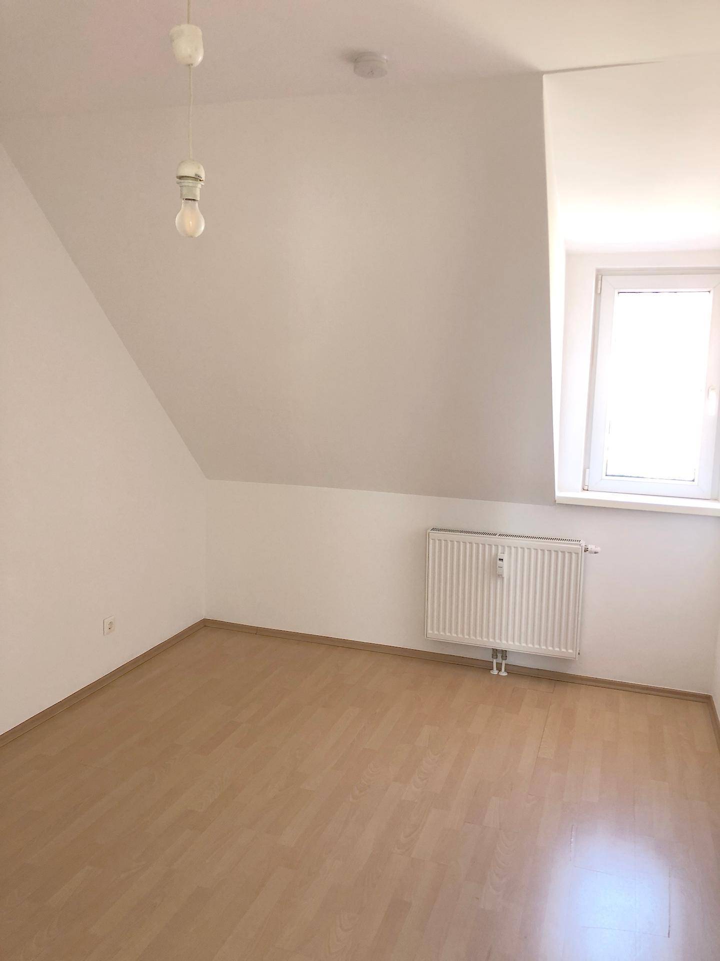 Schlafzimmer mit Laminatboden, Dachschräge und Fenster für natürliches Licht.