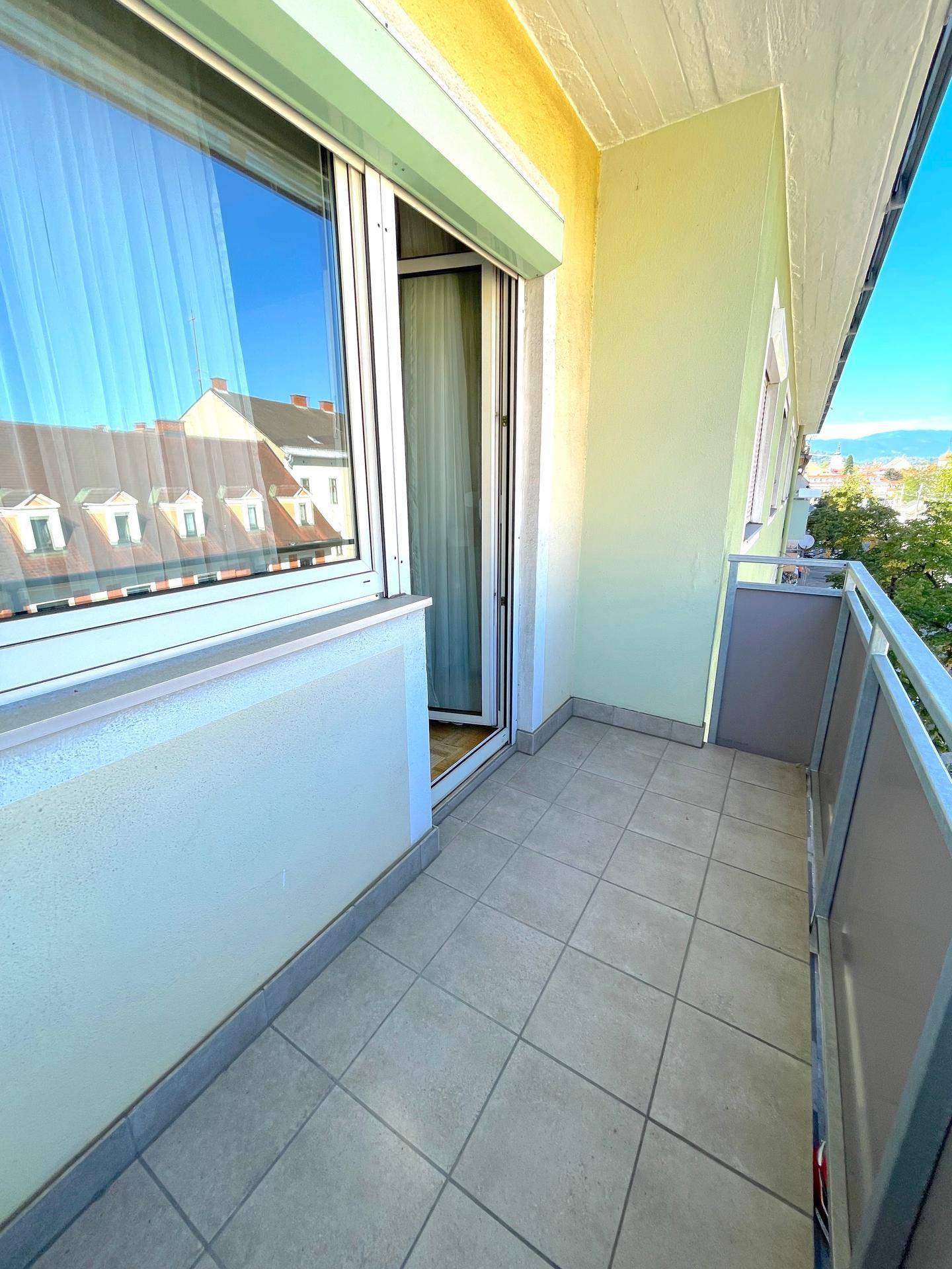 Sonniger Balkon mit Fliesenboden und Blick auf die Stadt und die umliegende Landschaft.
