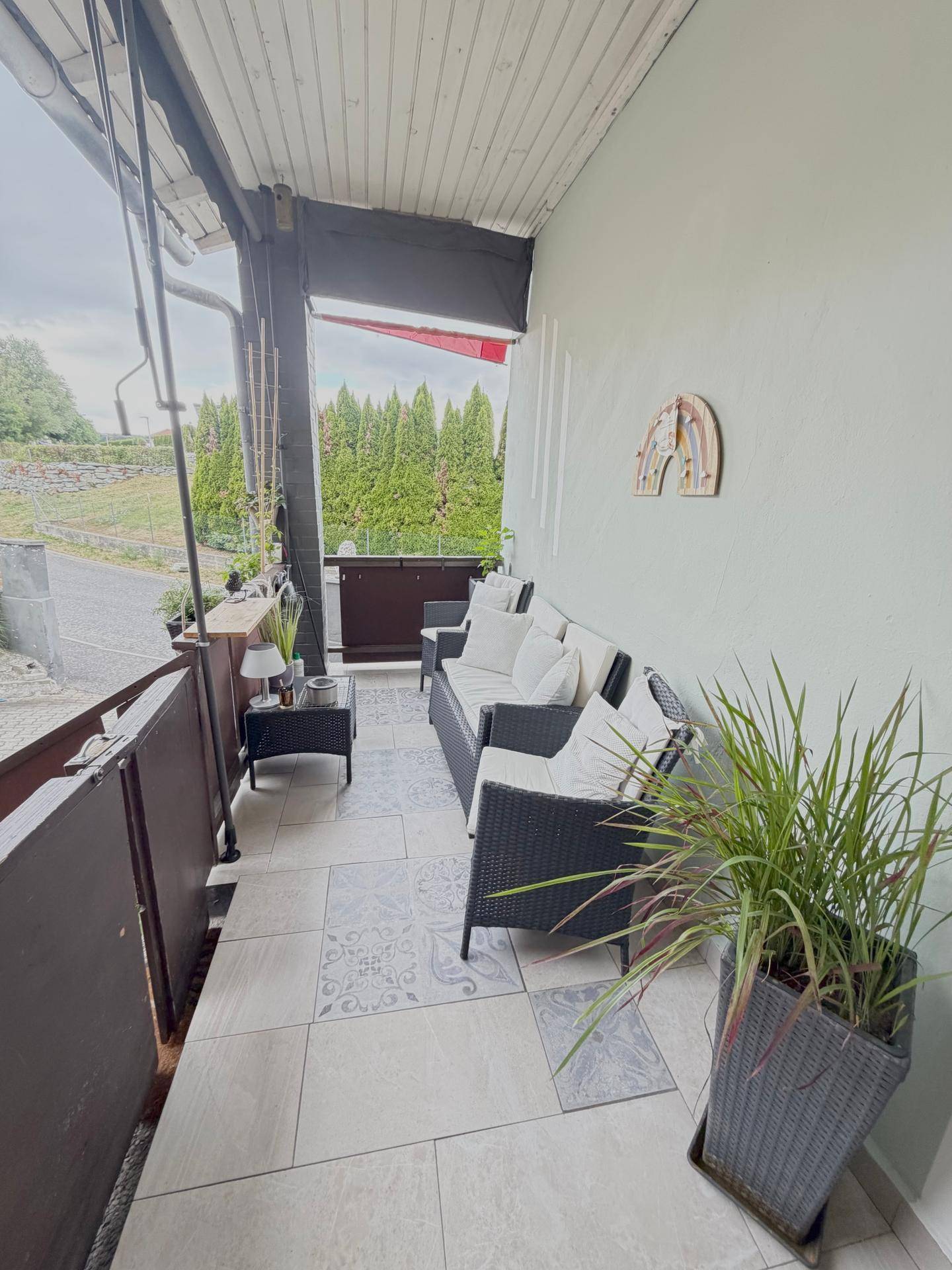 Gemütlicher Balkon mit Sitzmöbeln, Fliesenboden und Blick ins Grüne.