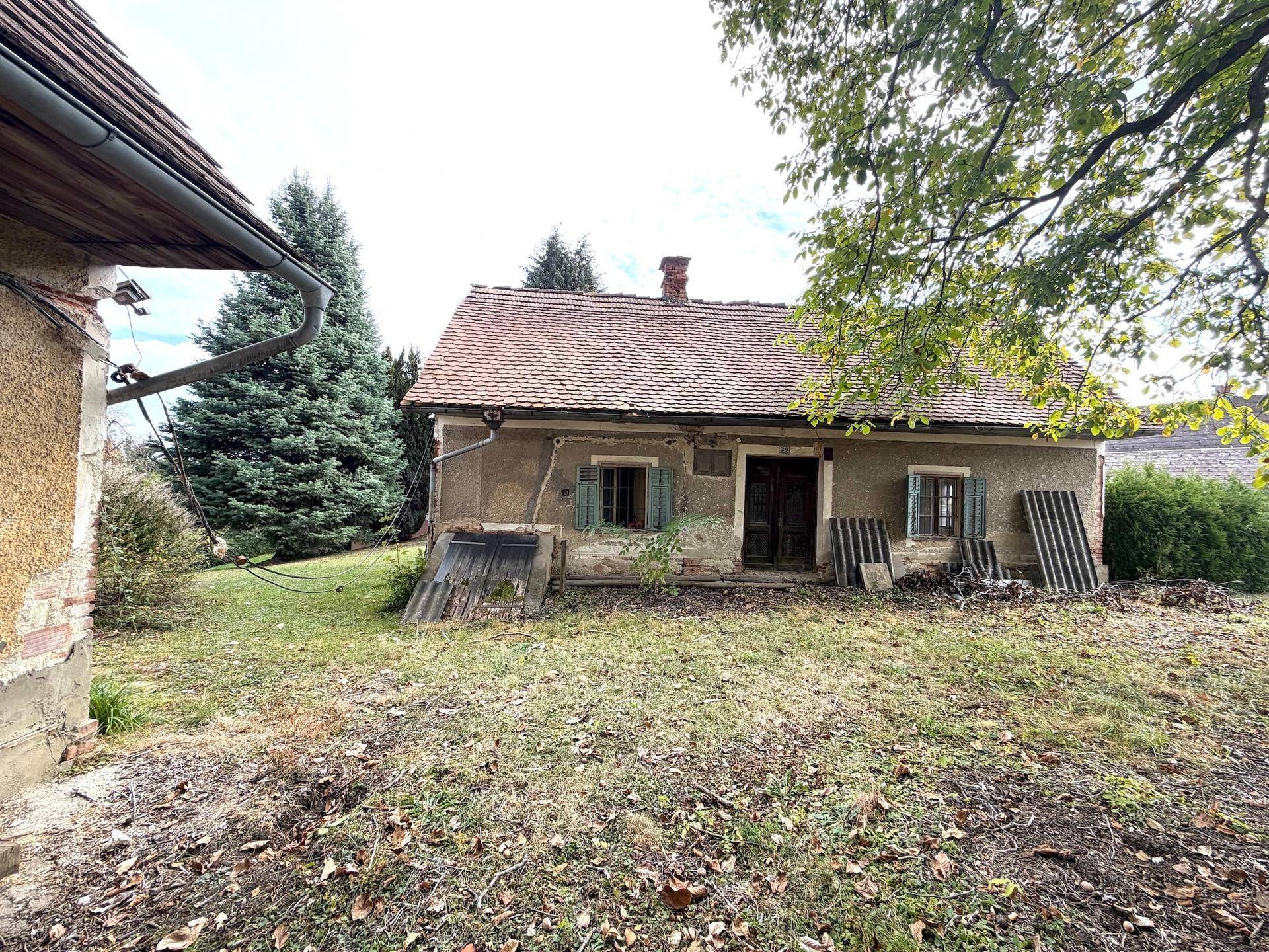 Vorderansicht des renovierungsbedürftigen Hauses mit verwitterter Fassade und alten Fensterläden.