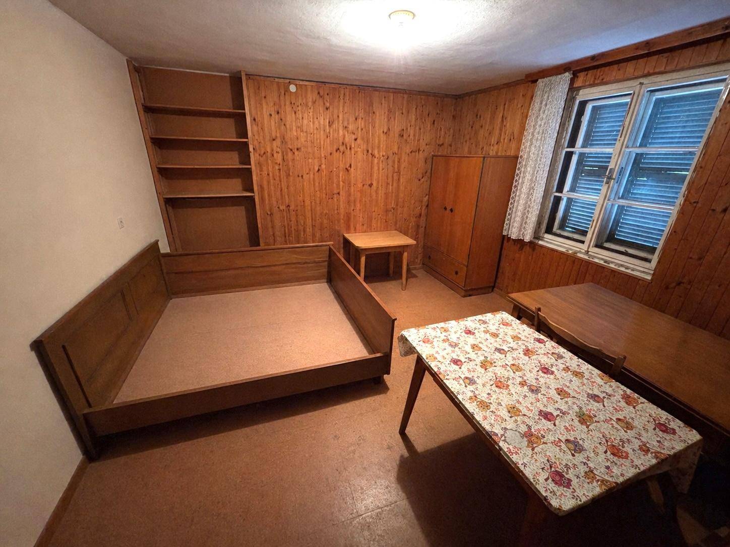 Schlafzimmer mit Holzvertäfelung, Bettrahmen, Kleiderschrank und kleinem Tisch.