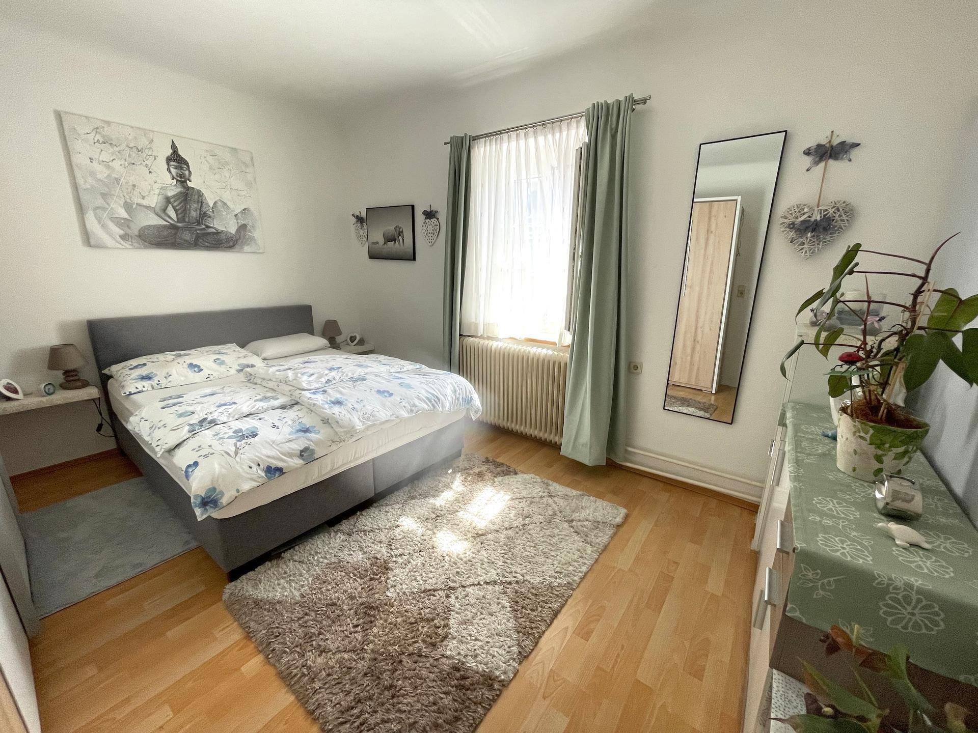 Schlafzimmer mit Doppelbett, Laminatboden, großem Fenster und modernem Dekor.