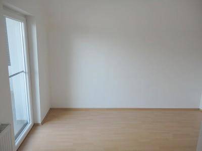 Leerer Raum mit Laminatboden und großem Fenster, bereit zur individuellen Gestaltung.