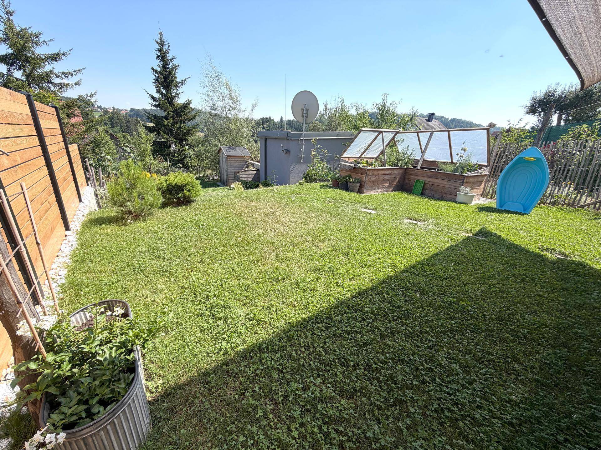 Grüner Gartenbereich mit Rasenfläche, Hochbeeten und einem kleinen Geräteschuppen.