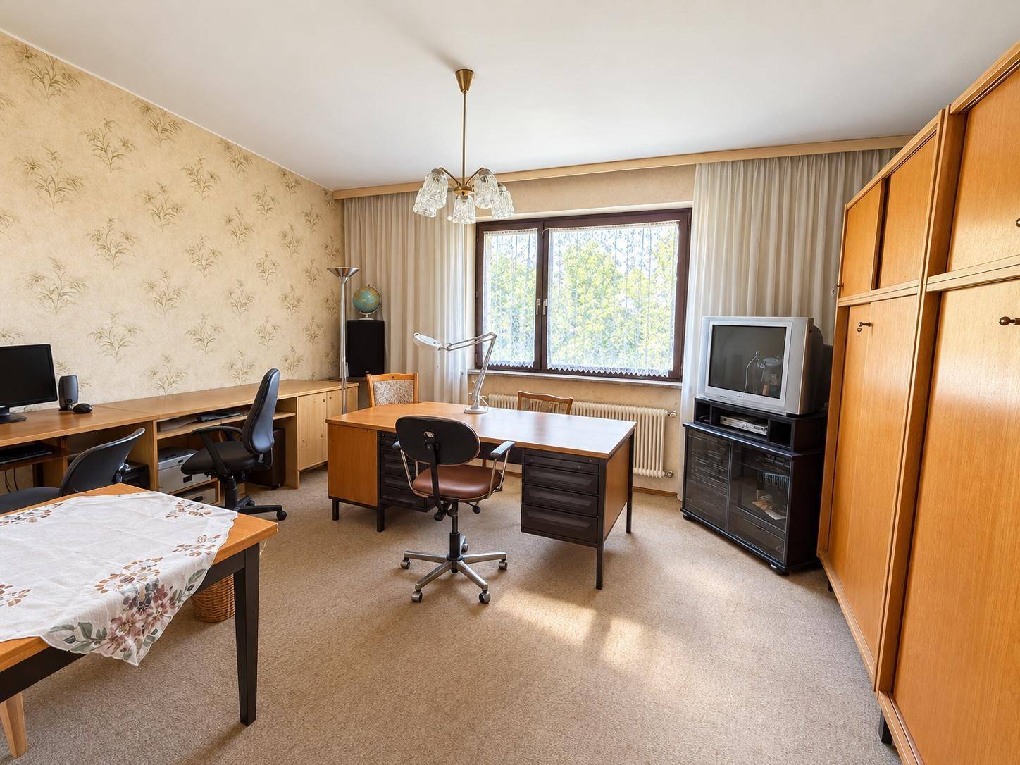 Geräumiges Arbeitszimmer mit Teppichboden, Holzmöbeln und Blick ins Grüne.