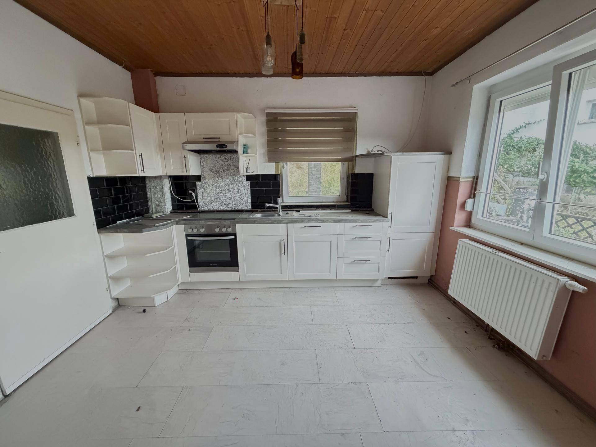 Küche mit weißen Schränken, schwarzem Fliesenspiegel und Fenster, ausgestattet mit einem Herd.