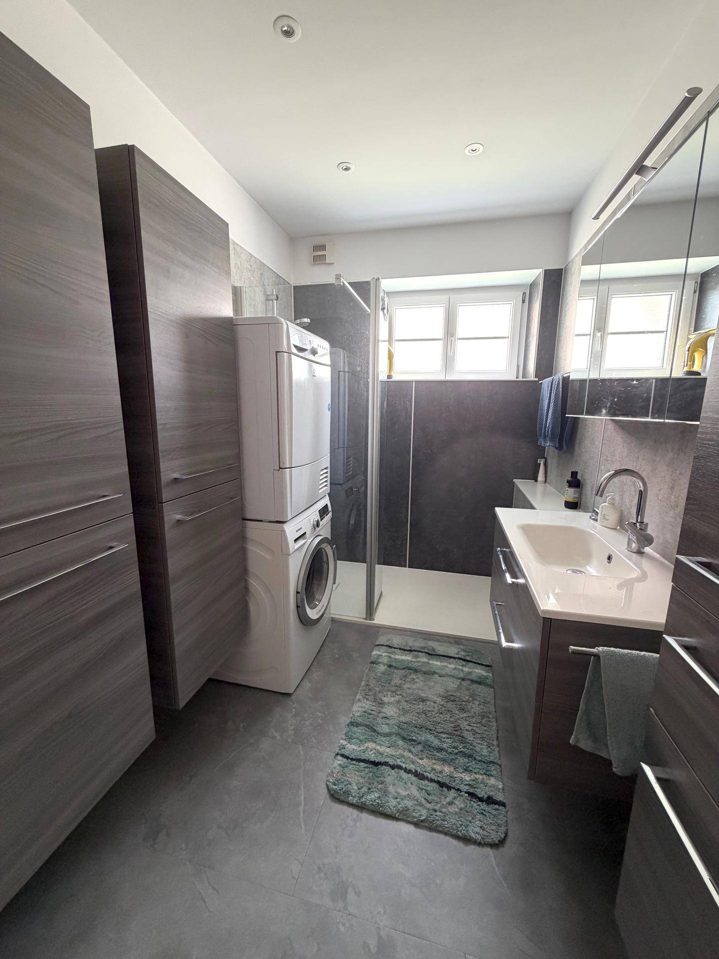 Modernes Badezimmer mit Dusche, Waschbecken, Waschmaschine und Trockner.