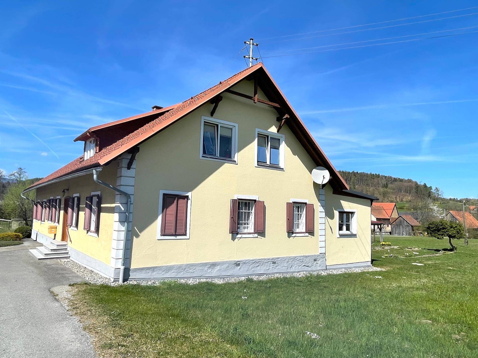 Seitenansicht eines gelben Hauses mit rotem Ziegeldach und braunen Fensterläden unter blauem Himmel.