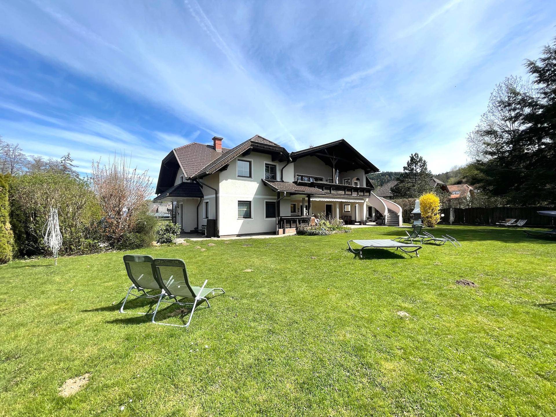 Die Rückseite des Hauses mit einem großen Rasen und Liegestühlen unter blauem Himmel.