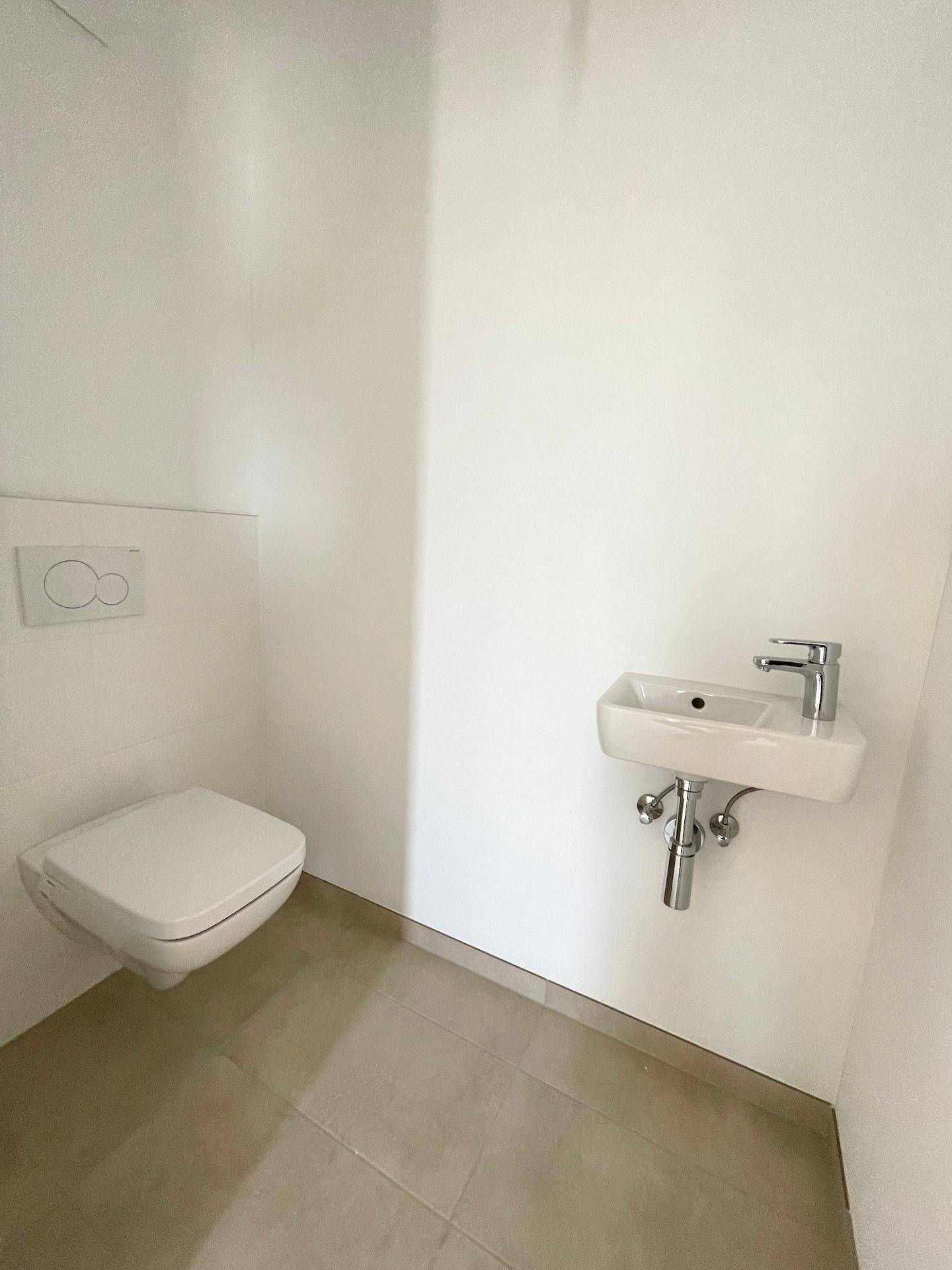 Modernes Gäste-WC mit wandhängendem WC und kleinem Waschbecken auf hellem Fliesenboden.