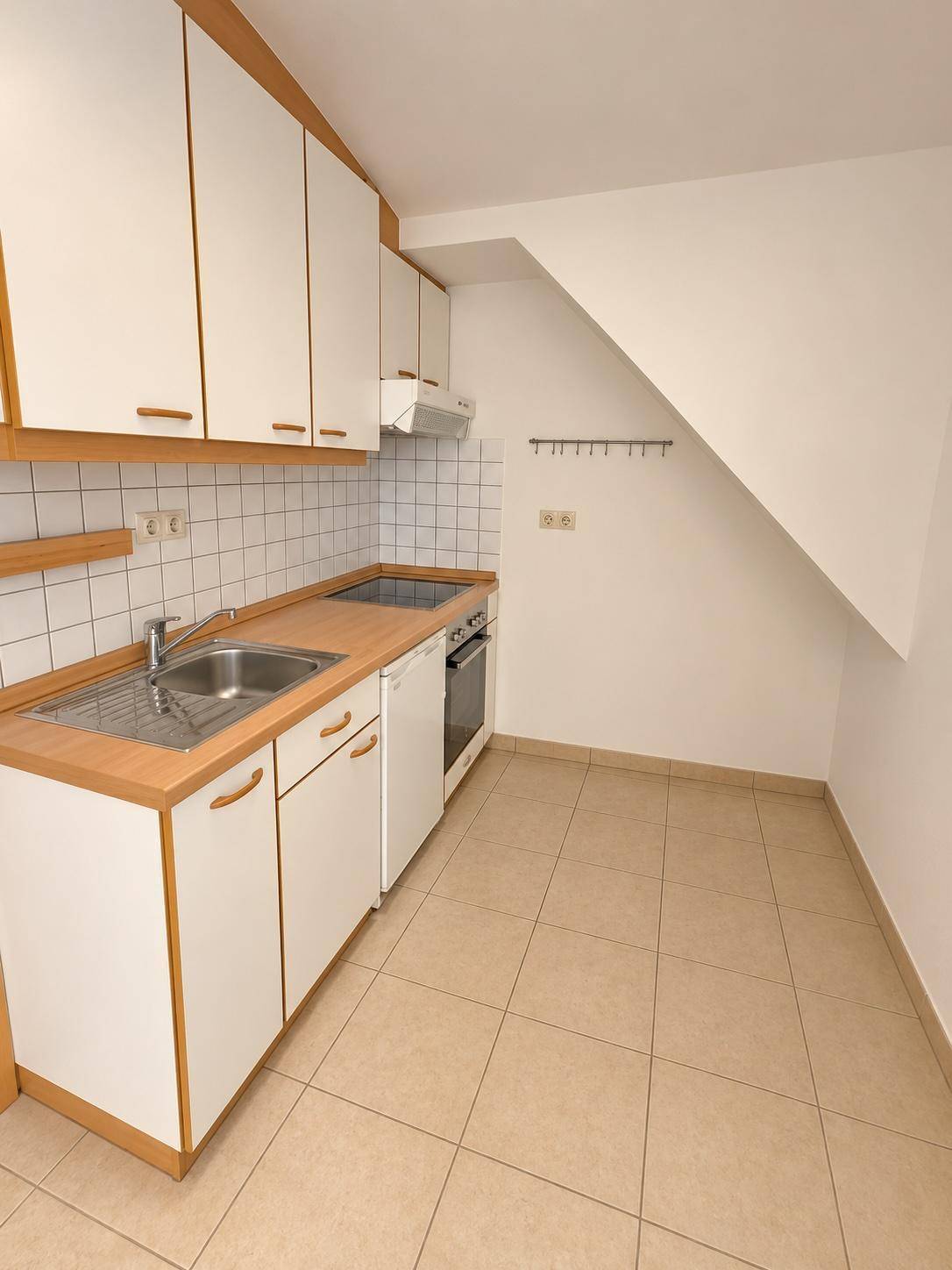 Kompakte Einbauküche mit weißen Fronten, Holz-Arbeitsplatte und integriertem Herd unter der Dachschräge.
