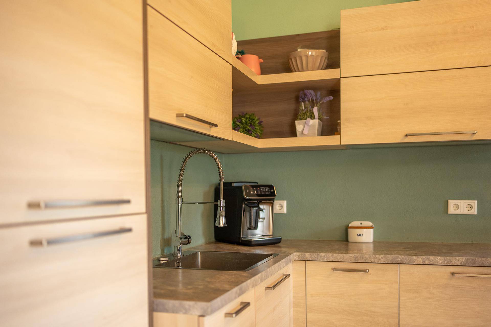 Detailansicht der modernen Küche mit Holzelementen, Spüle und integrierter Kaffeemaschine.
