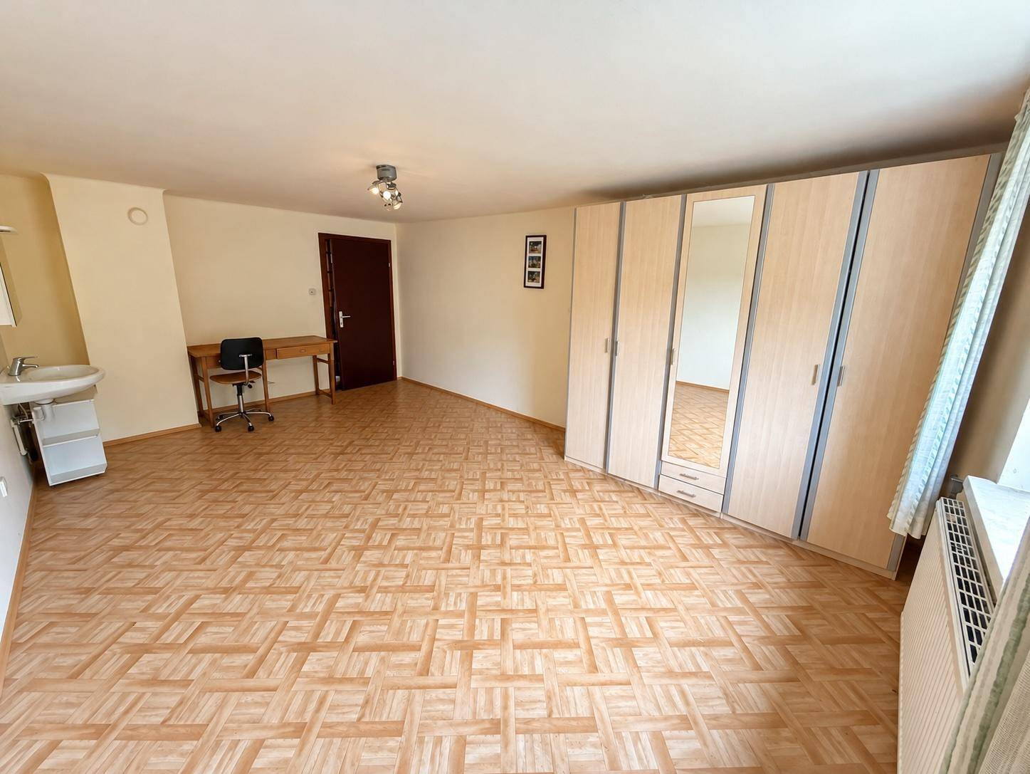 Geräumiges Zimmer mit Laminatboden, Einbauschränken und Waschbecken.
