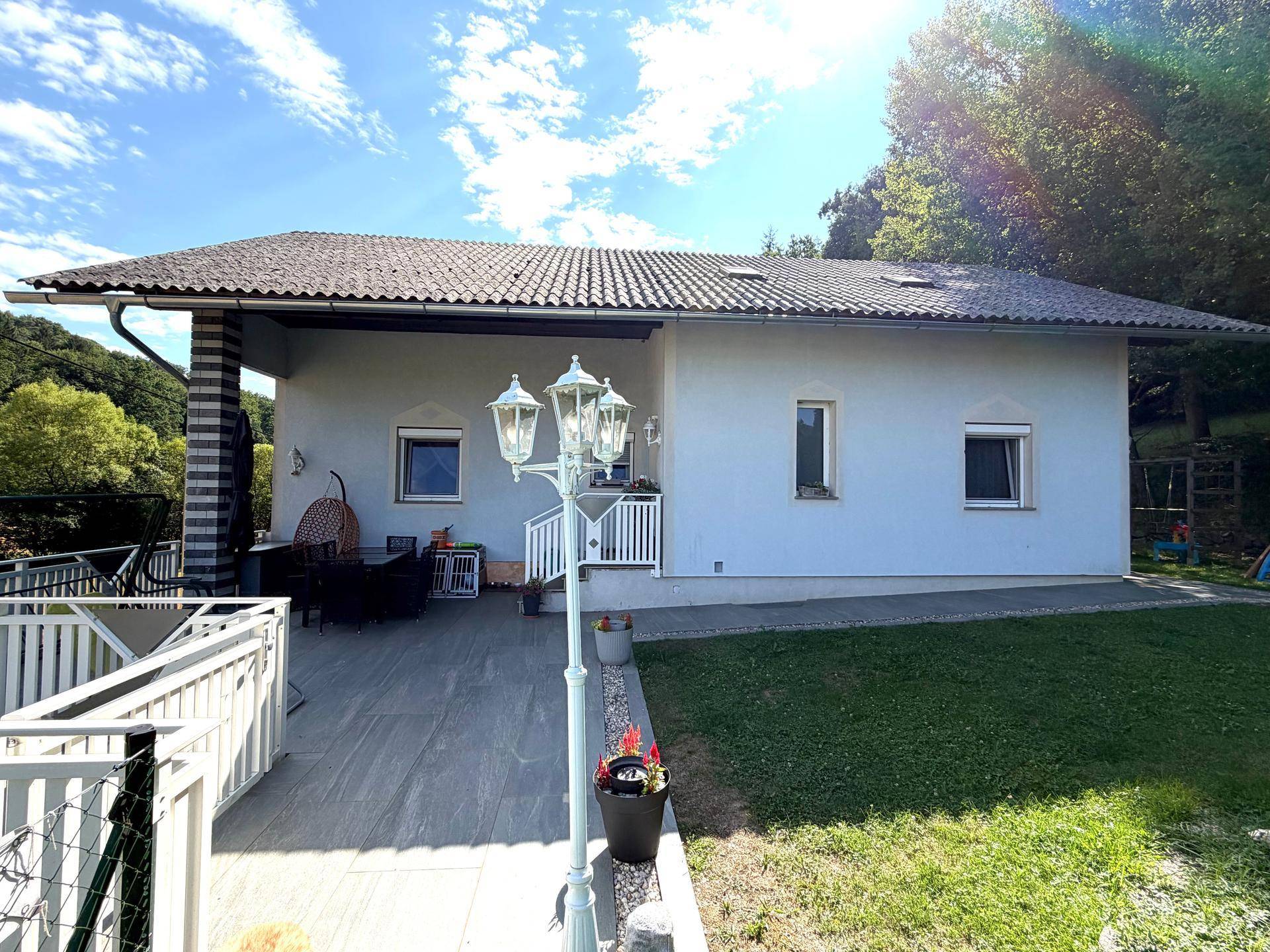 Geräumige, gepflasterte Terrasse vor dem Haus mit dekorativer Laterne und Blick ins Grüne.