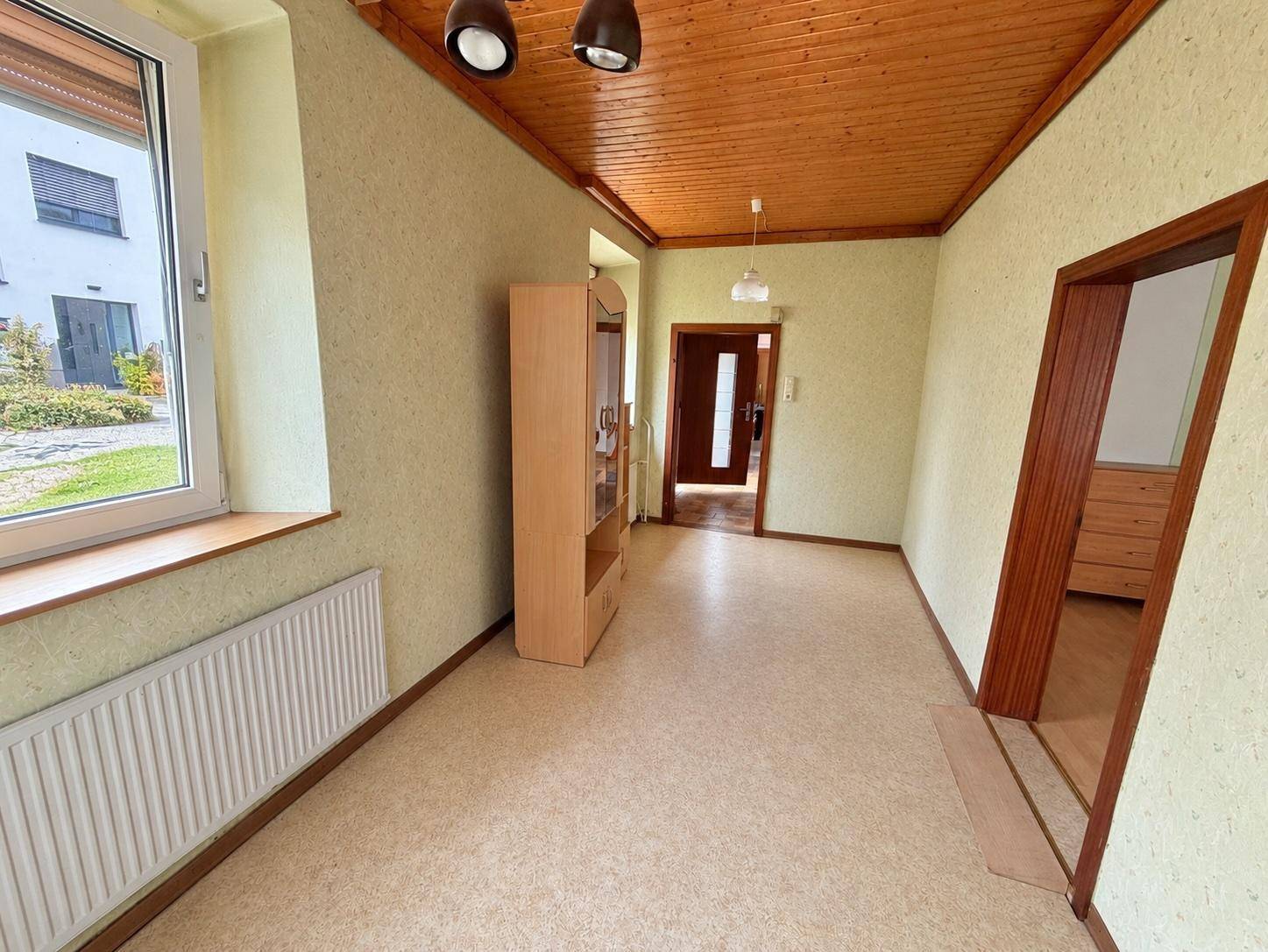 Heller Raum mit Holzdecke, Tapeten und Fenster mit Blick auf den Garten.