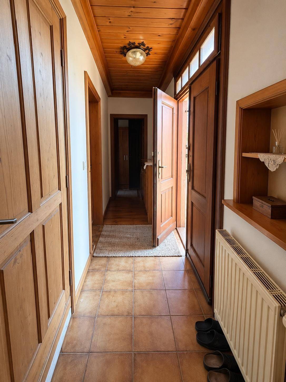 Heller Flur mit Holzdecke, Fliesenboden und Holztüren, der zu weiteren Räumen führt.