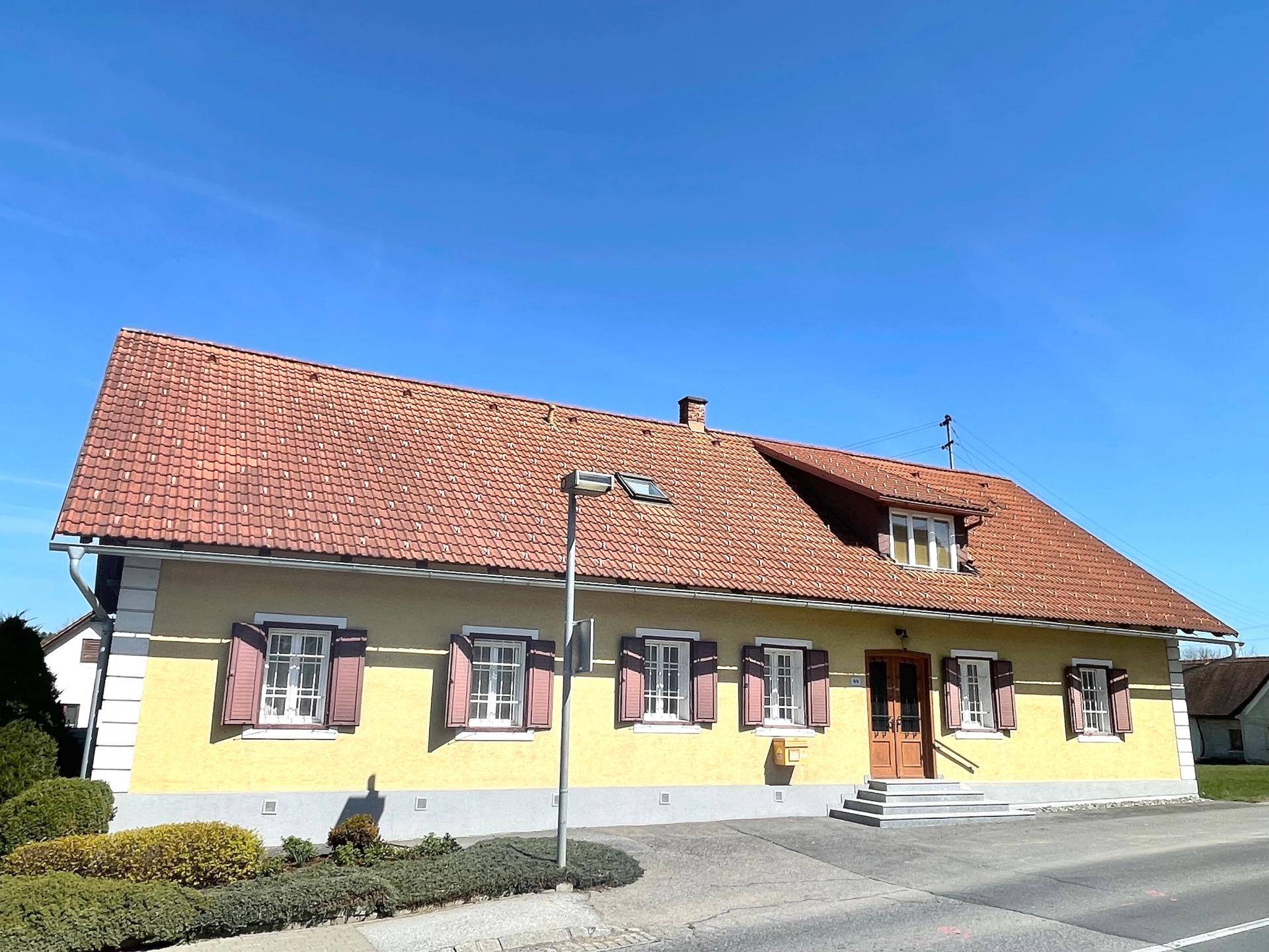 Vorderansicht des gelben Hauses mit rotem Dach, Fensterläden und Eingangsbereich.