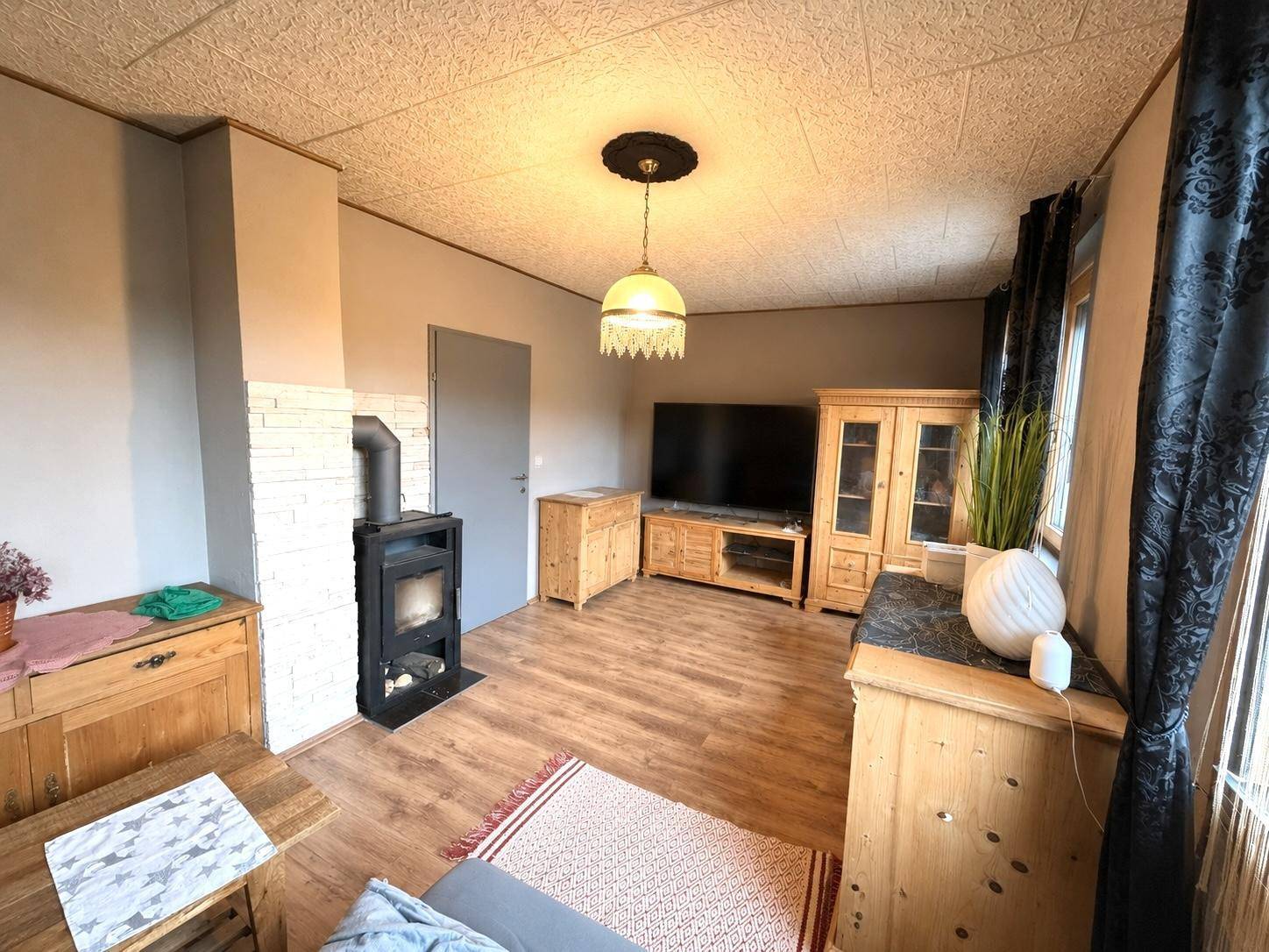 Wohnzimmer mit Holzboden, Kaminofen und rustikalen Holzmöbeln, gemütlich eingerichtet.