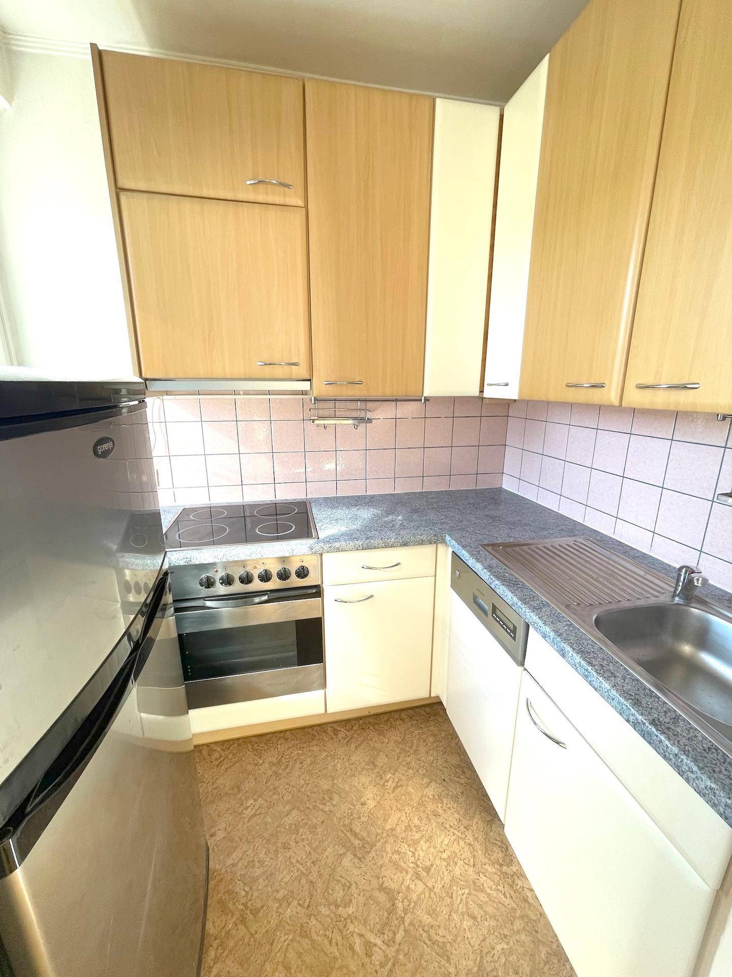 Funktionale Küche mit hellen Holzschränken, Fliesenrückwand und integrierten Geräten.