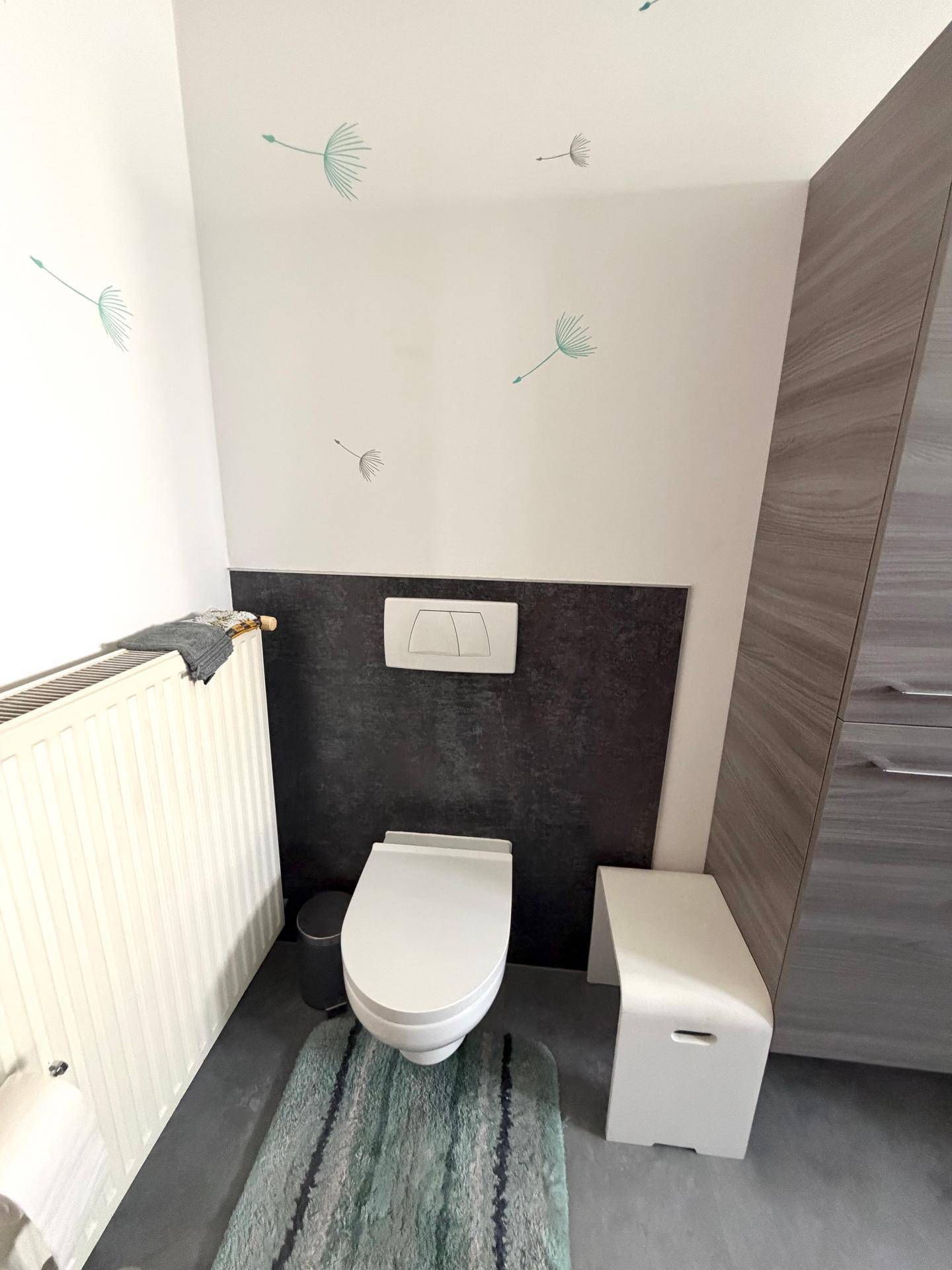 Modernes WC mit wandhängender Toilette und dunklen Fliesen.