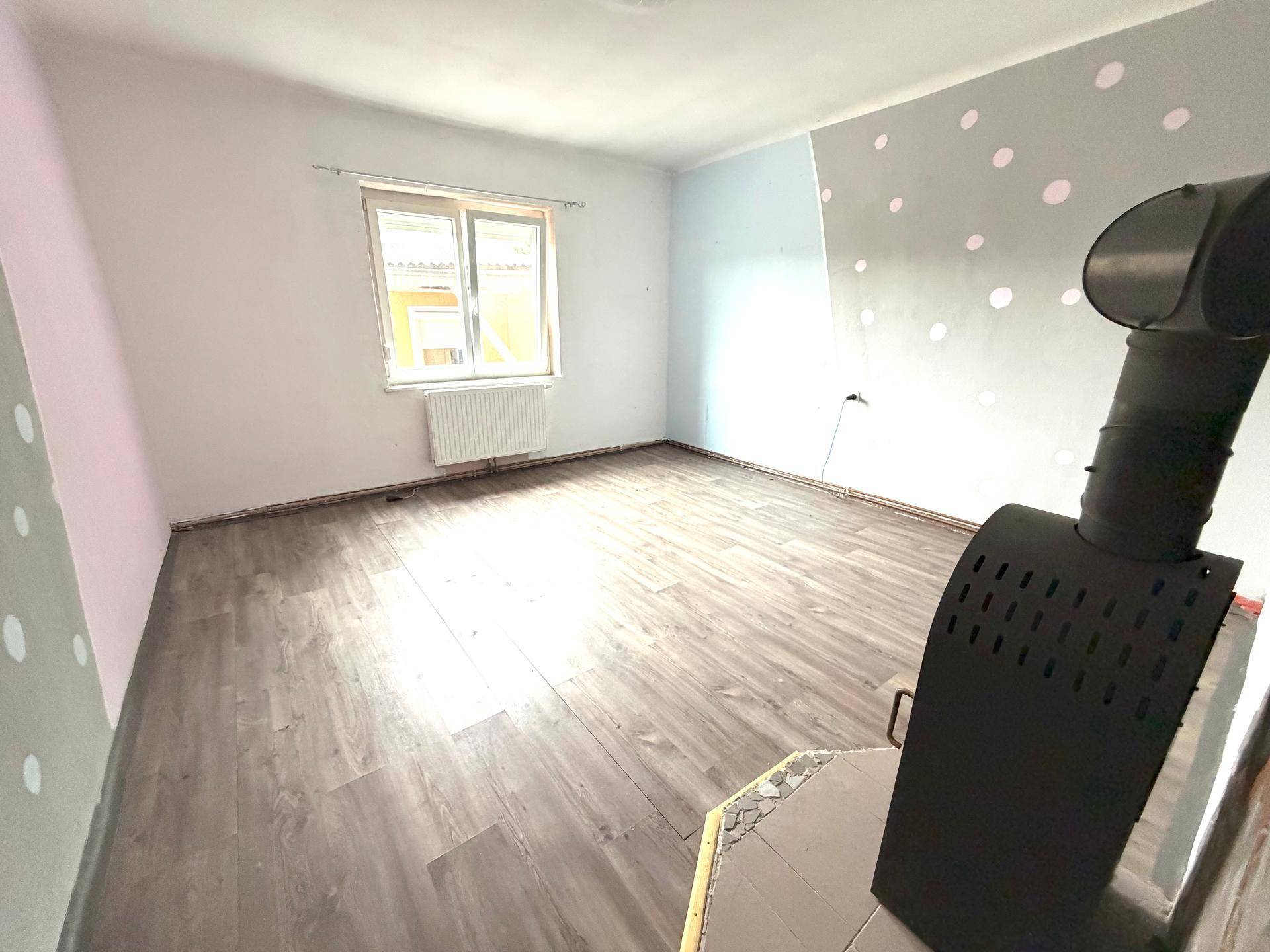 Leeres Zimmer mit Laminatboden, Holzofen und farblich gestalteten Wänden.