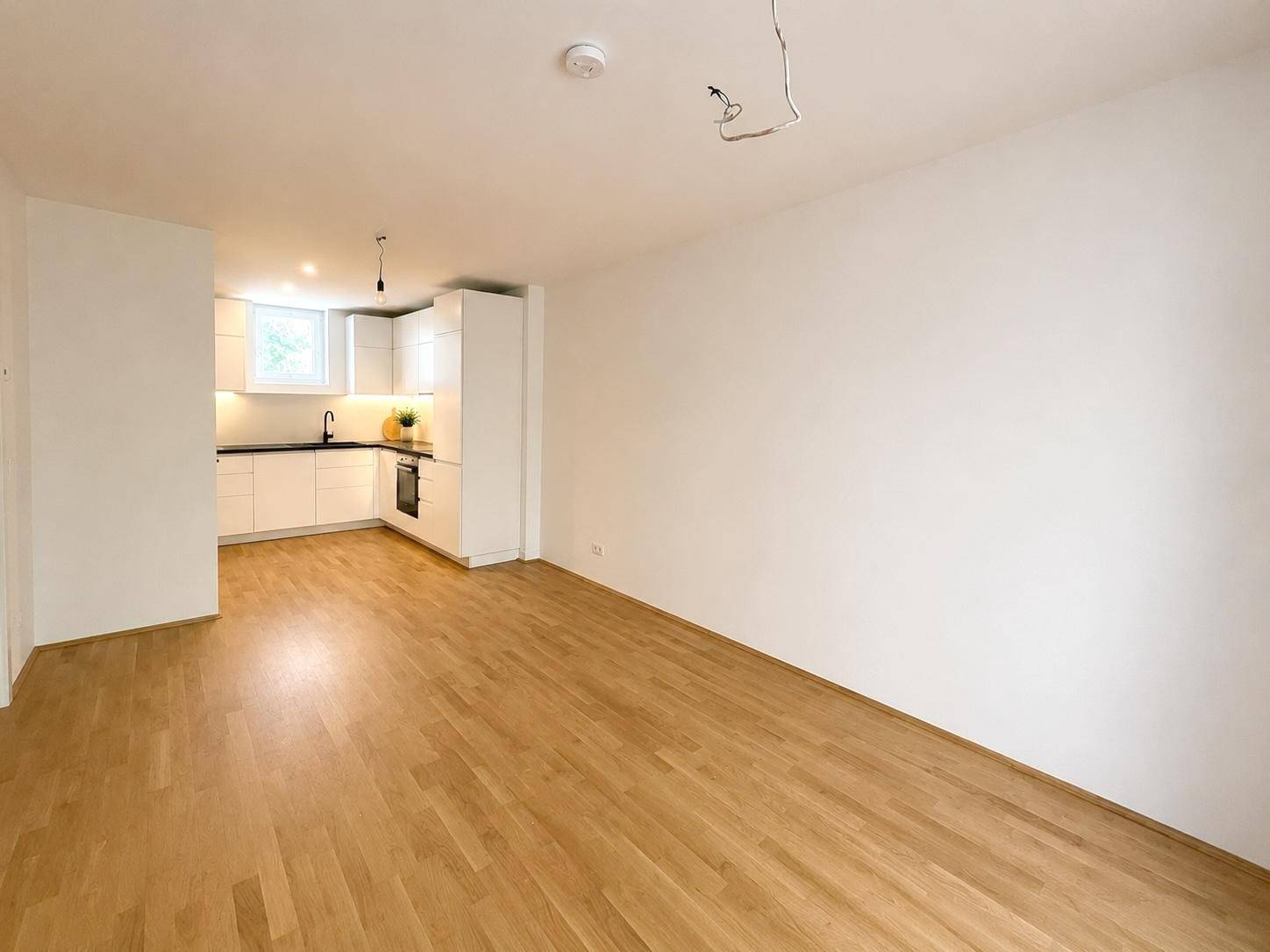Heller offener Wohnbereich mit integrierter Küche und durchgehendem Holzfußboden, ideal für modernes Wohnen.