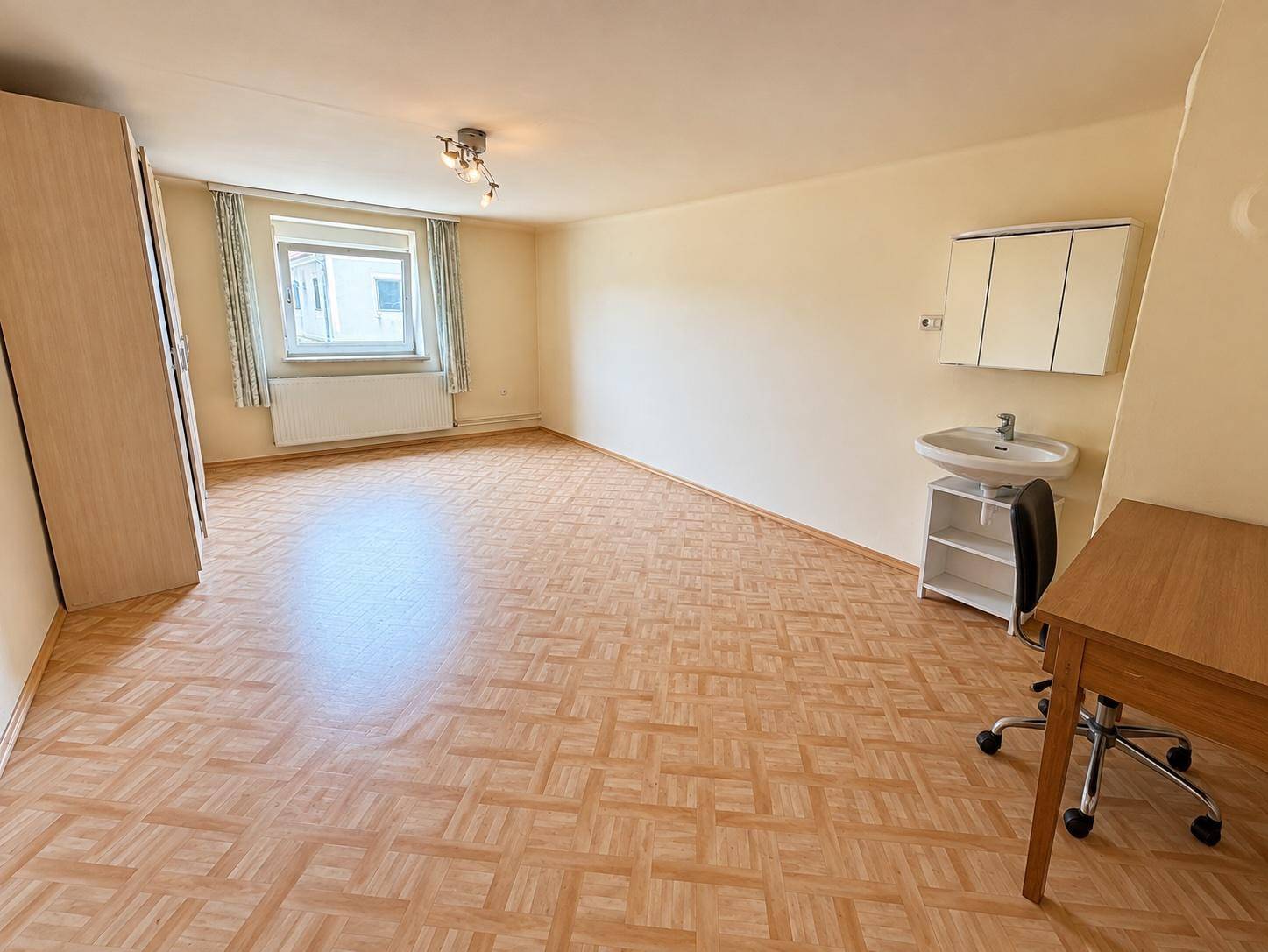 Großes Zimmer mit Laminatboden, Waschbecken und Kleiderschrank.