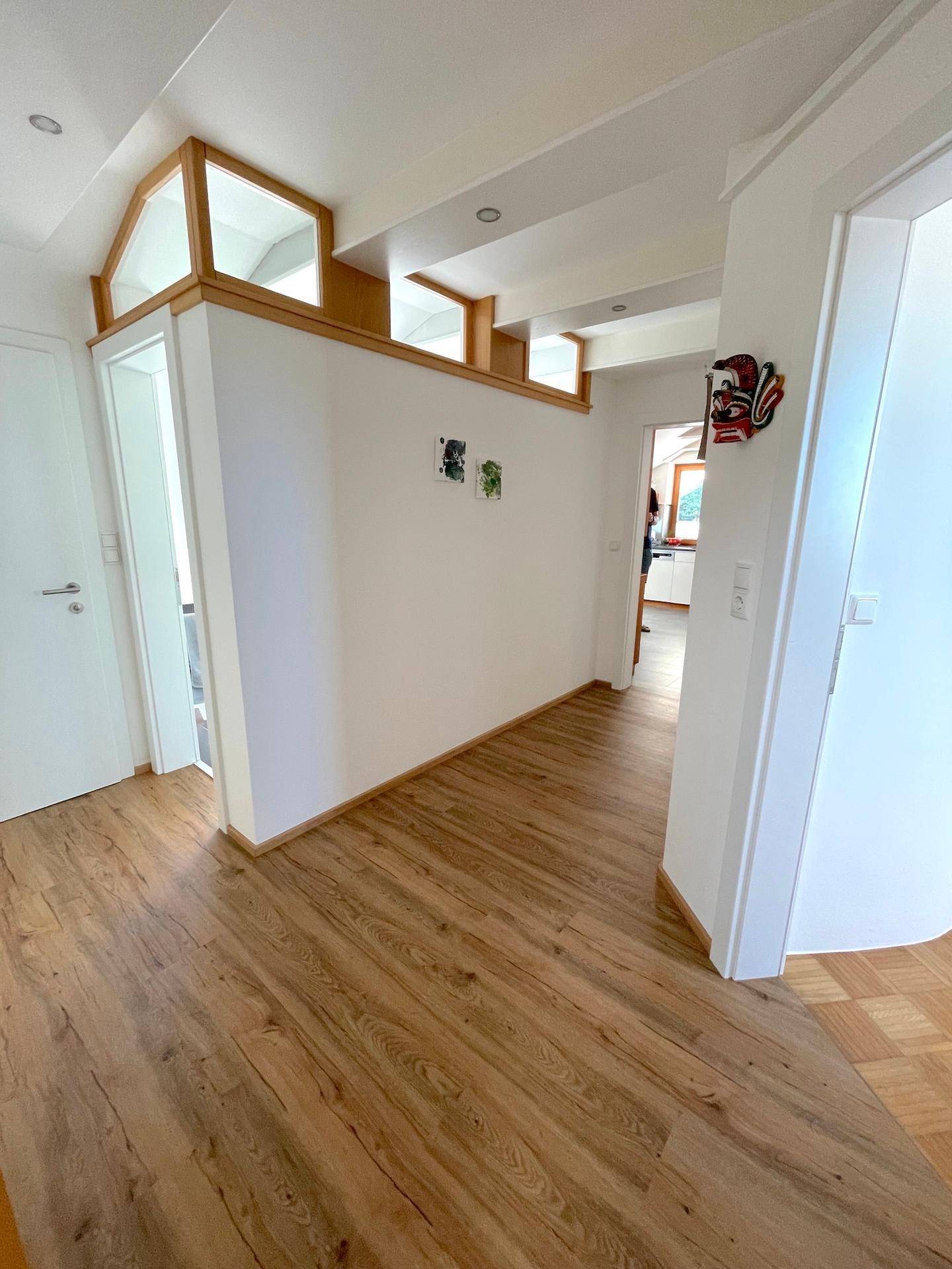 Geräumiger Flur mit Holzfußboden, weißen Wänden und interessanten architektonischen Deckendetails.
