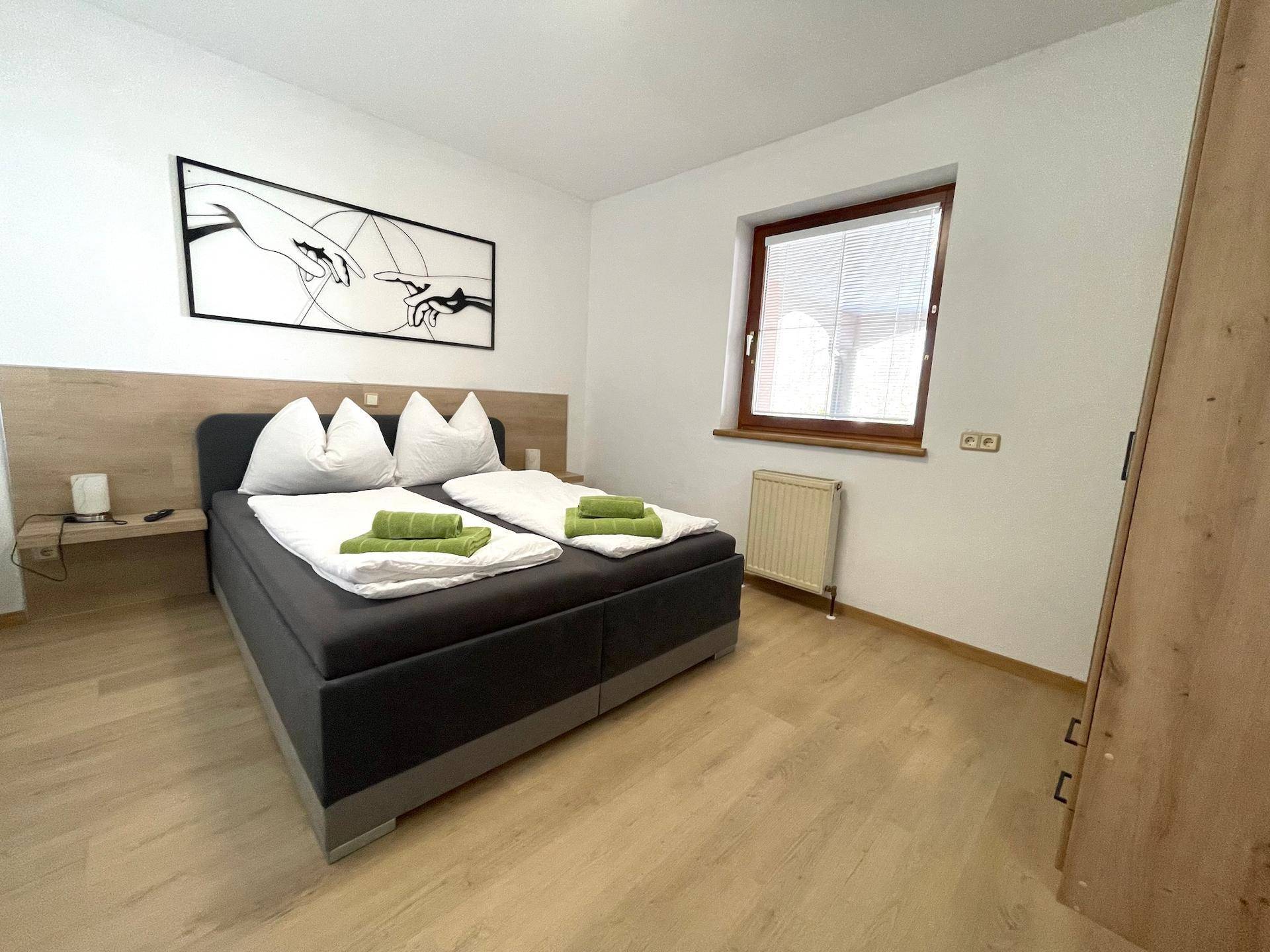 Ein helles Schlafzimmer mit Doppelbett, Laminatboden und minimalistischer Dekoration.