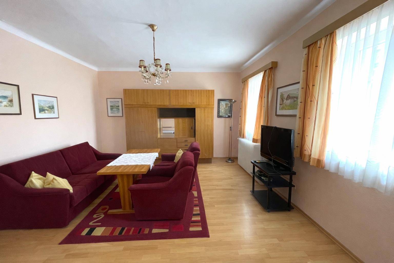 Gemütliches Wohnzimmer mit Holzboden, roter Sitzgruppe und einem großen Schrank.