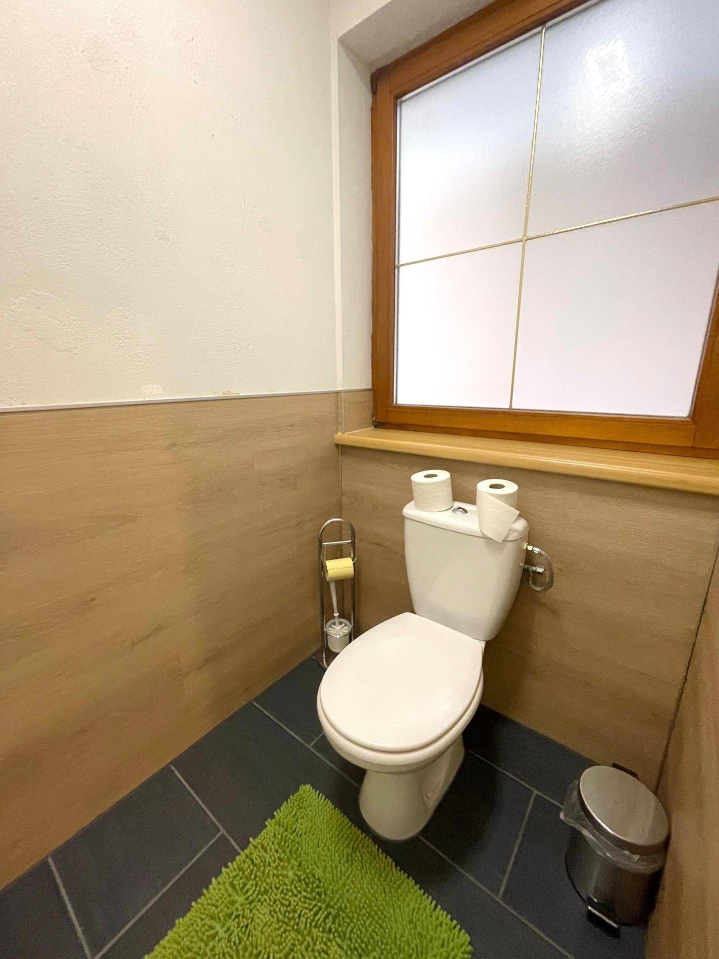 Eine moderne Gästetoilette mit Fenster, dunklen Bodenfliesen und Holzvertäfelung.