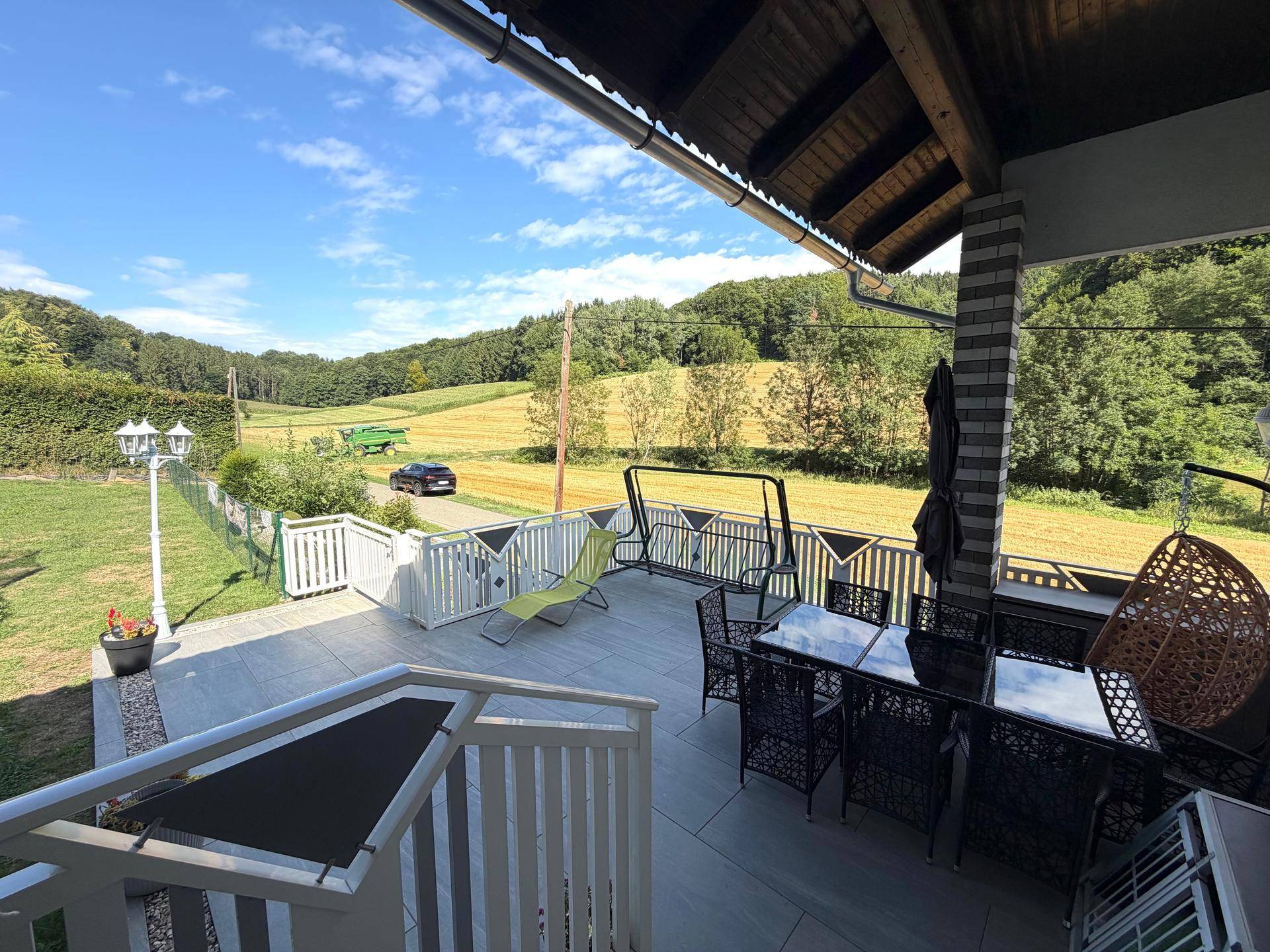 Große Terrasse mit Gartenmöbeln und Blick auf die umliegende grüne Landschaft und Felder.