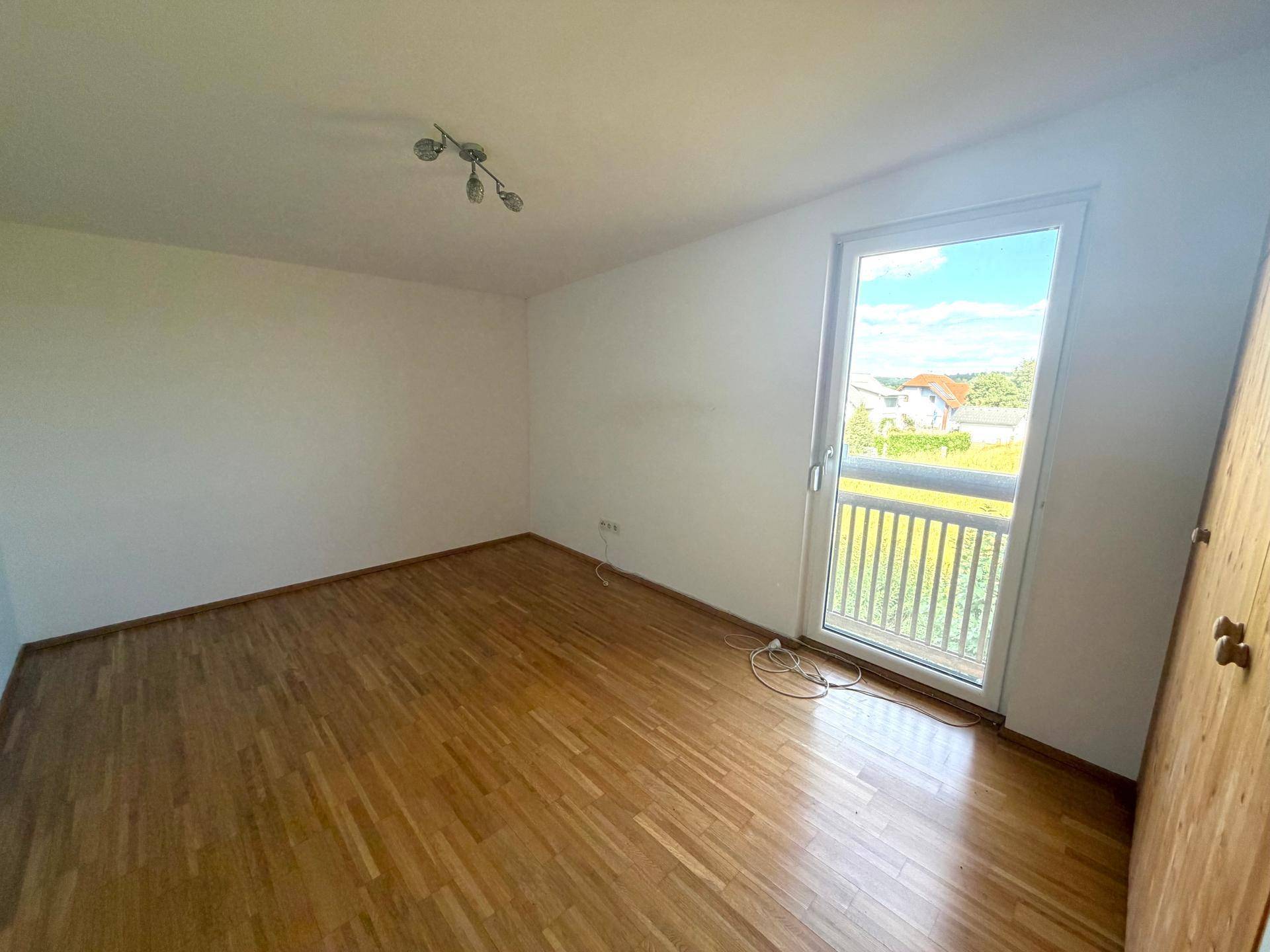 Helles Schlafzimmer mit Holzboden und Zugang zu einem französischen Balkon.