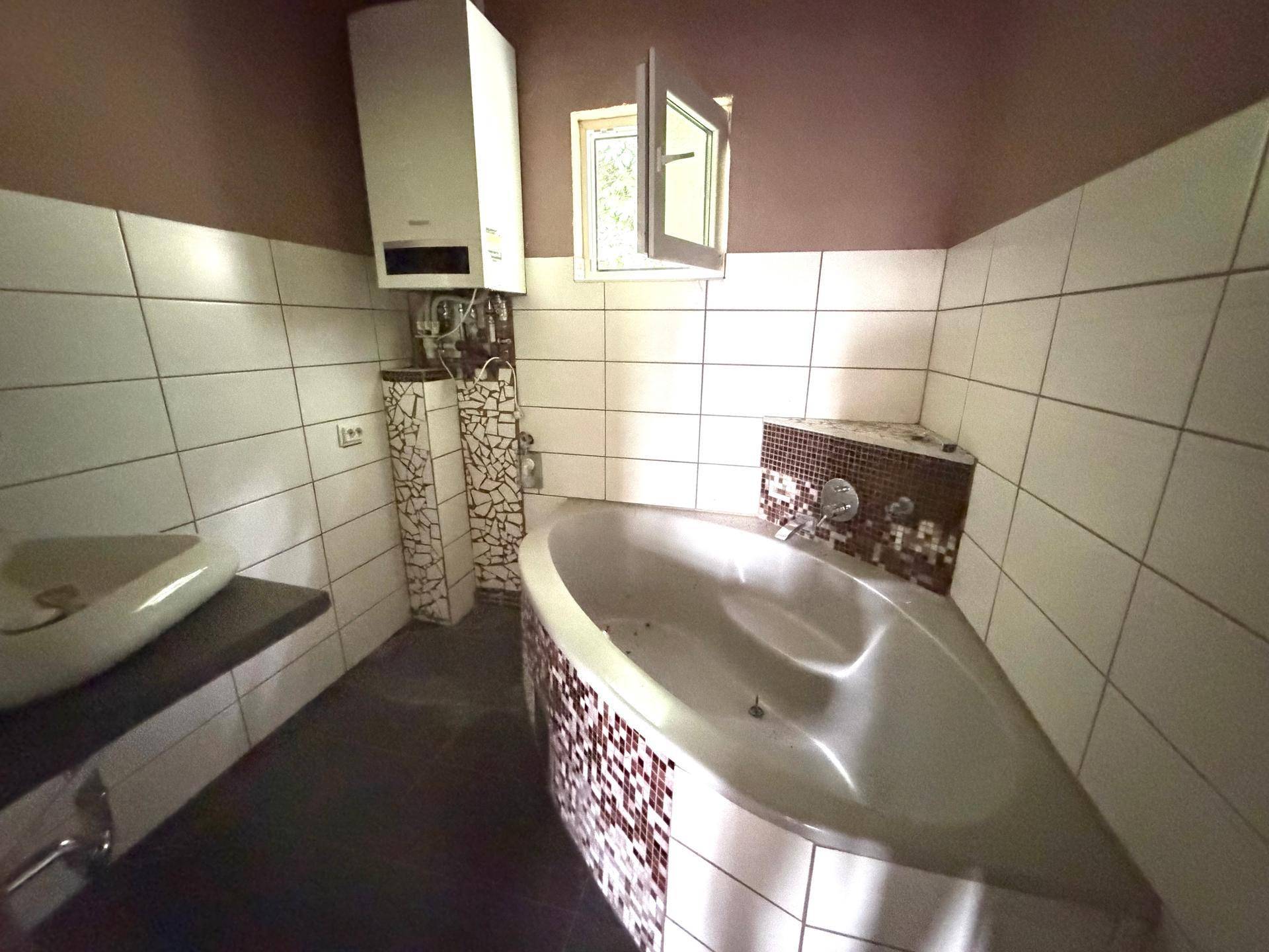 Badezimmer mit Badewanne, Waschbecken und Wandheizung, teilweise gefliest und mit Fenster.