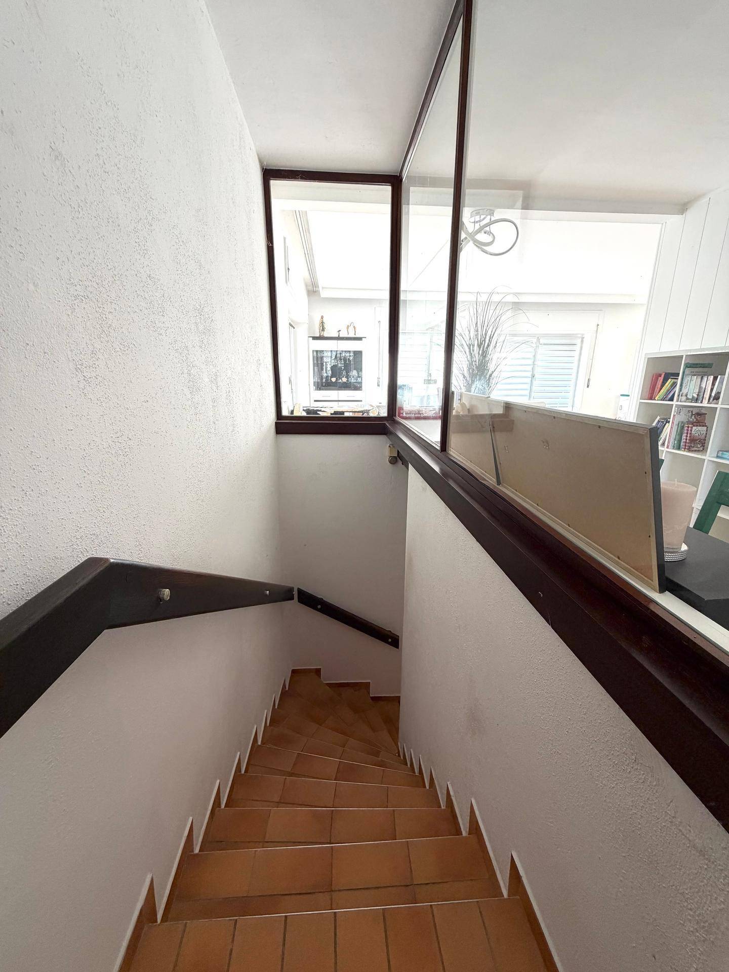 Treppenhaus mit Holzgeländer und Fliesenstufen, das die verschiedenen Ebenen verbindet.